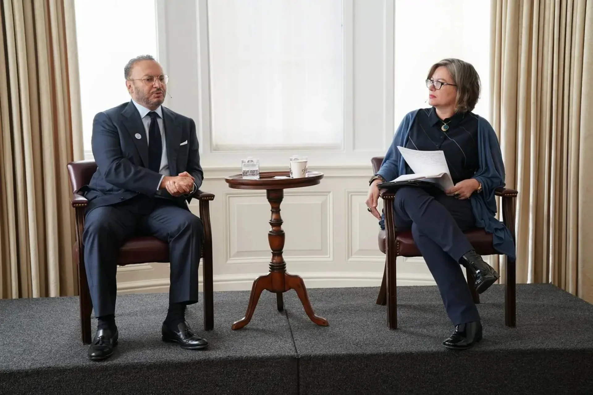 Photo of two people sitting in chairs on a stage.