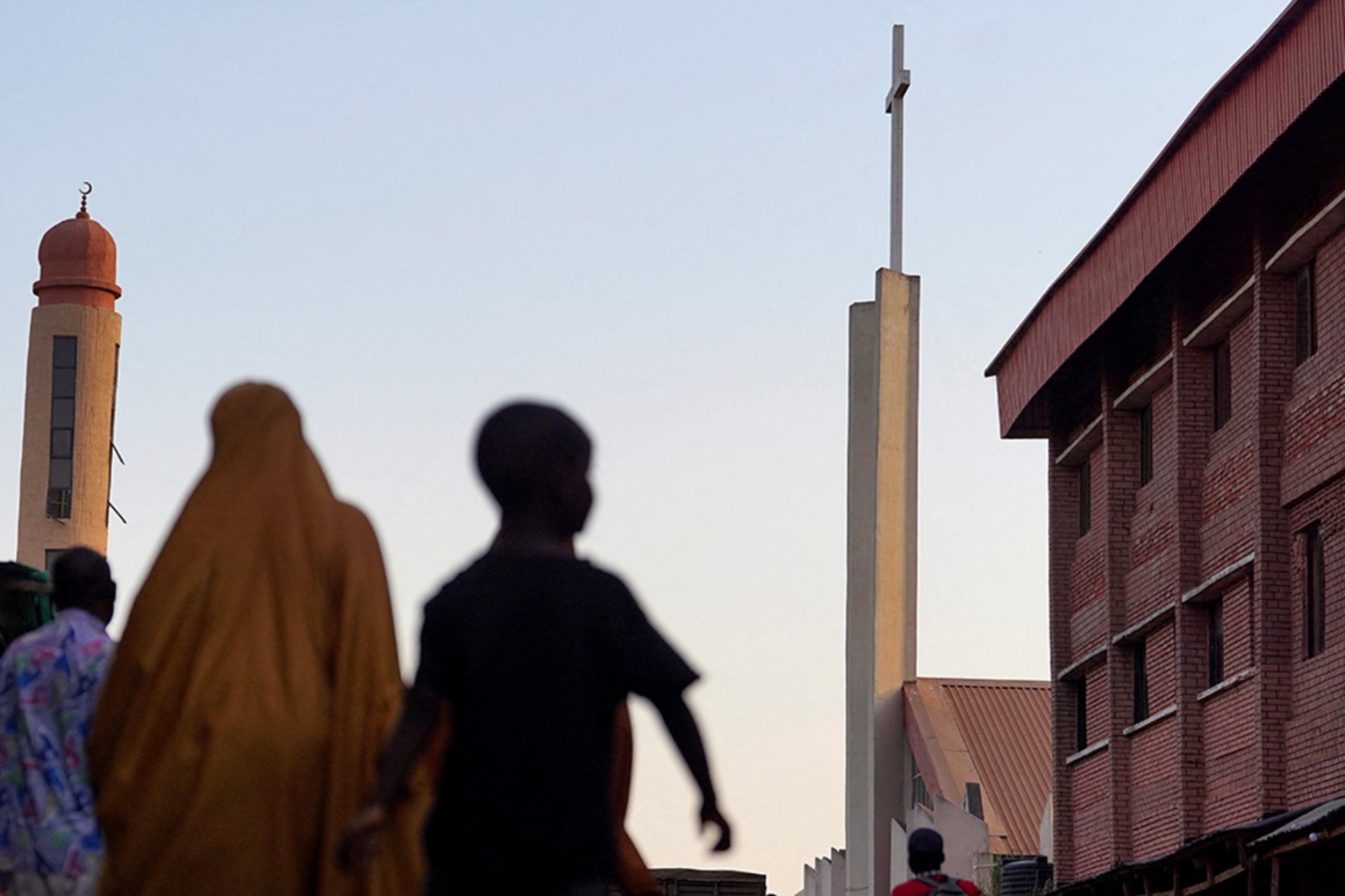<p>People walk along a street between St. Joseph Catholic Church and Kano Road Central Mosque in Kaduna, Nigeria. </p>
