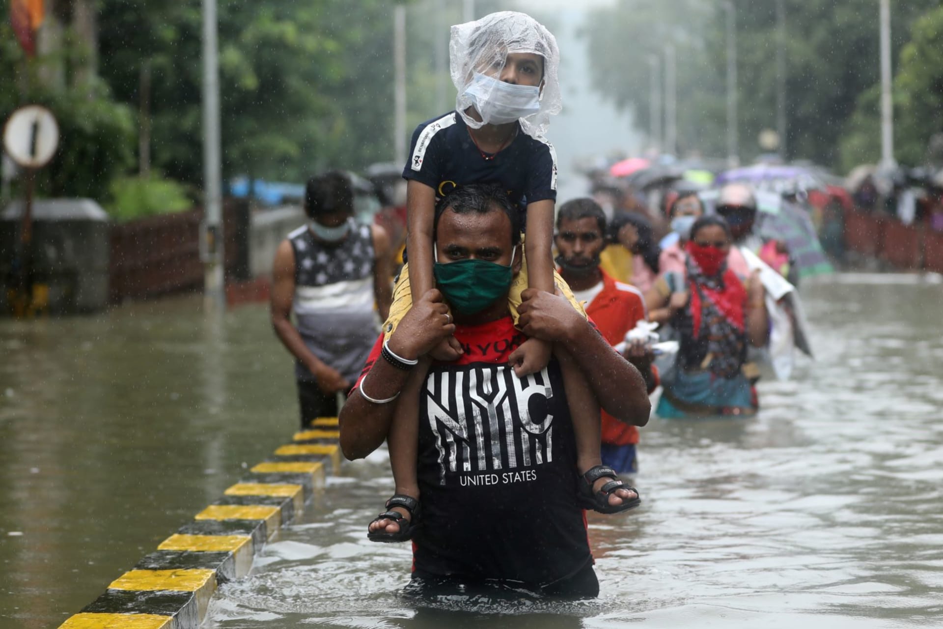<p>A man carries a child through a waterlogged road after heavy rainfall in Mumbai, India on September 23, 2020.</p>
