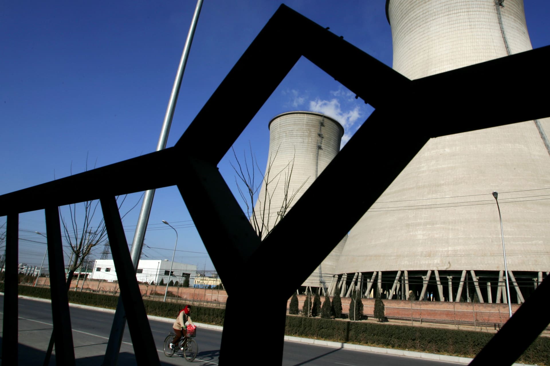 <p>A woman rides a bicycle past cooling towers at a thermal power plant in Beijing on December 3, 2007.</p>
