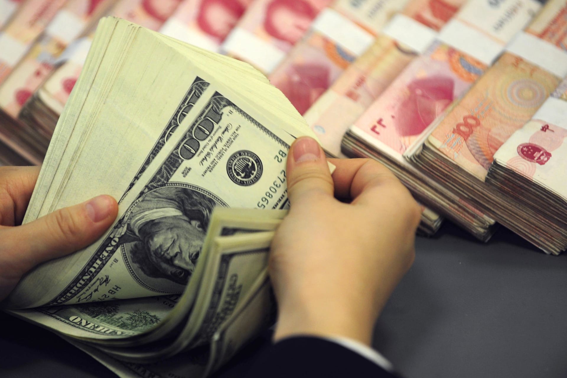<p>An employee counts U.S. currency near renminbi notes at a bank in Hefei, Anhui province, on December 3, 2008.</p>