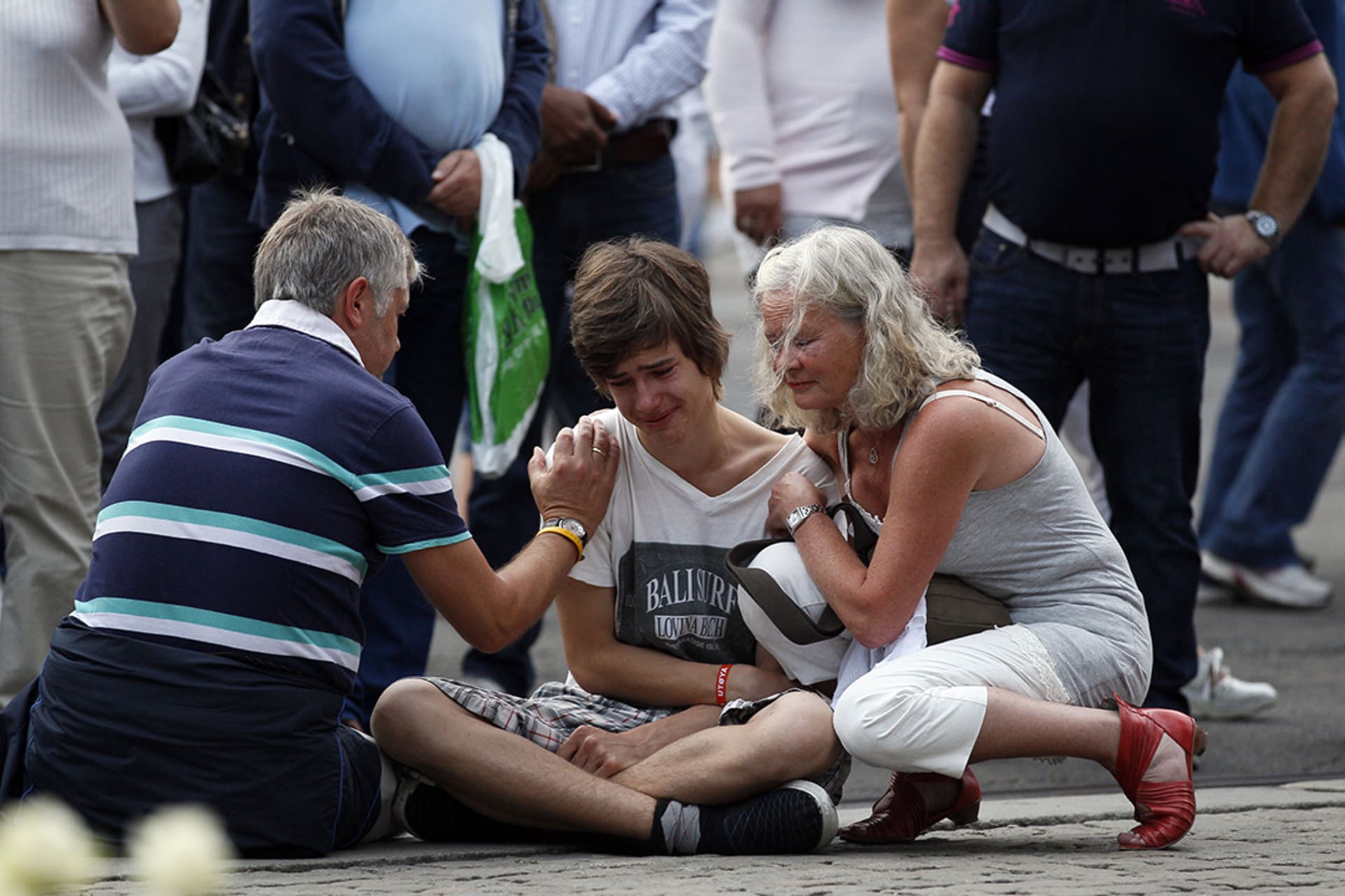 A young man is comforted as he mourns the deaths of those killed by Anders Breivik in a mass shooting and bombing in Norway. 
