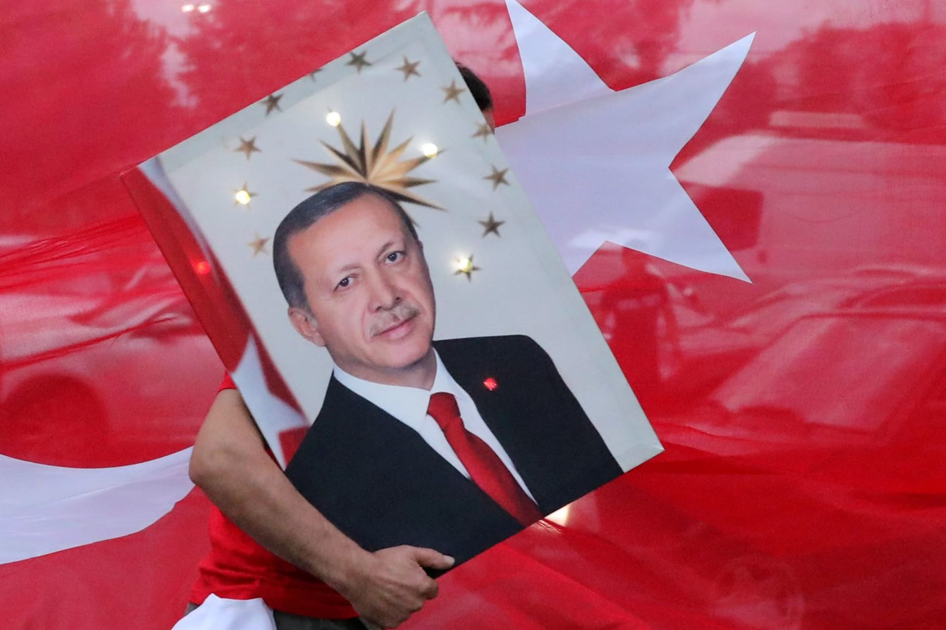 <p>A supporter of Turkish President Recep Tayyip Erdogan holds his picture in front of a Turkish flag in Istanbul.</p>