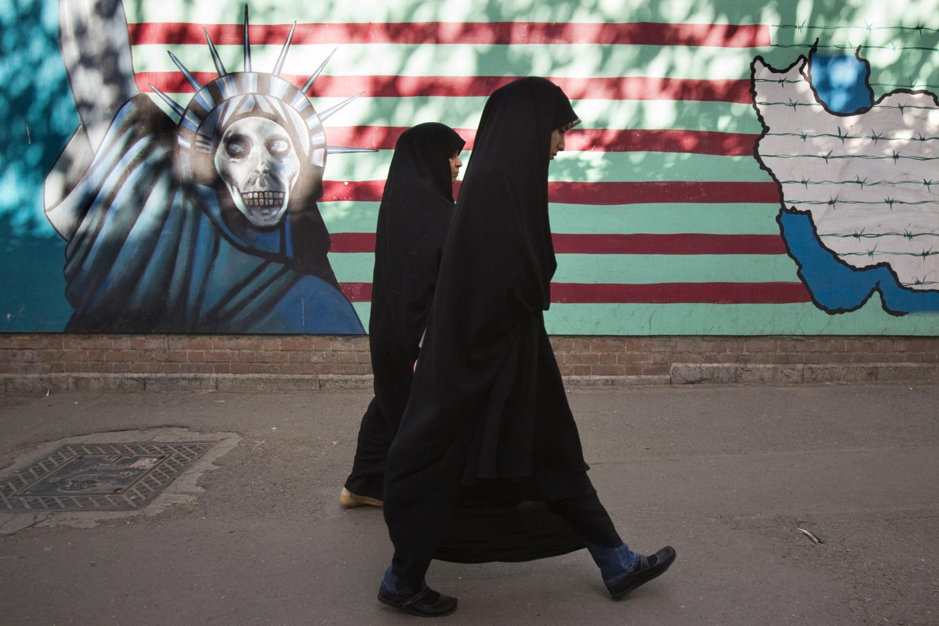 <p>Two Iranian women walk past a mural in Tehran.</p>
