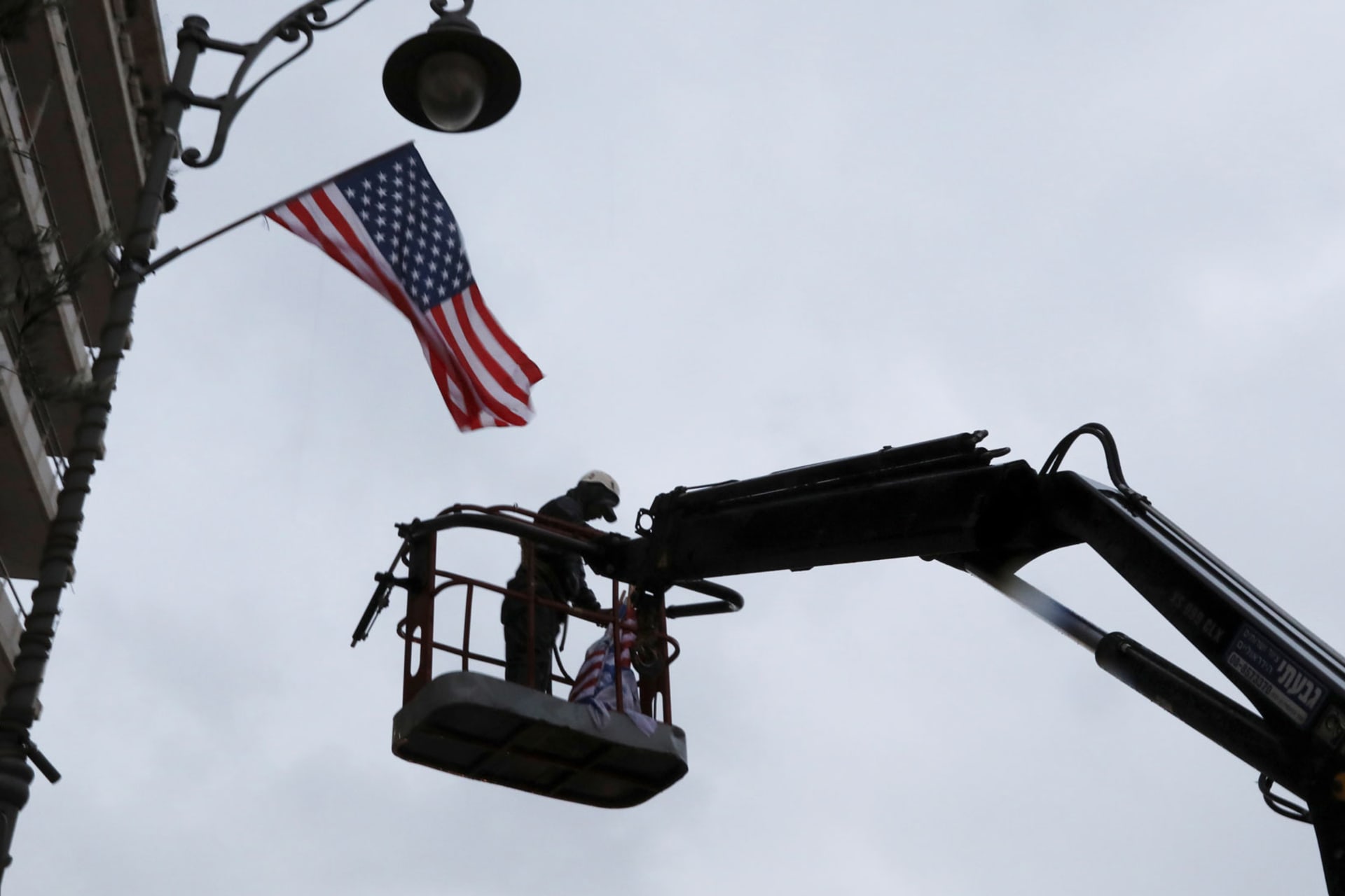 <p>A laborer hangs a U.S. national flag on a lamp post along a street where the U.S. consulate in located in Jerusalem on December 6, 2017. </p>

