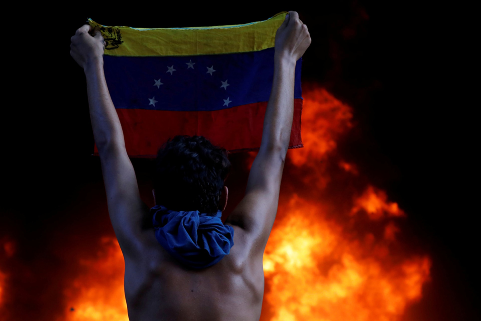 <p>A protestor holds a national flag while standing in front of a fire during a rally against Venezuela’s President Nicolas Maduro, in Caracas, Venezuela, on June 12, 2017.</p>