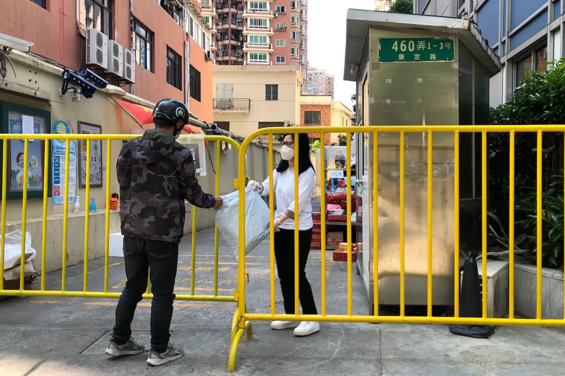 <p>A woman in Shanghai reaches through a barricade to receive a package delivery in May.</p>
