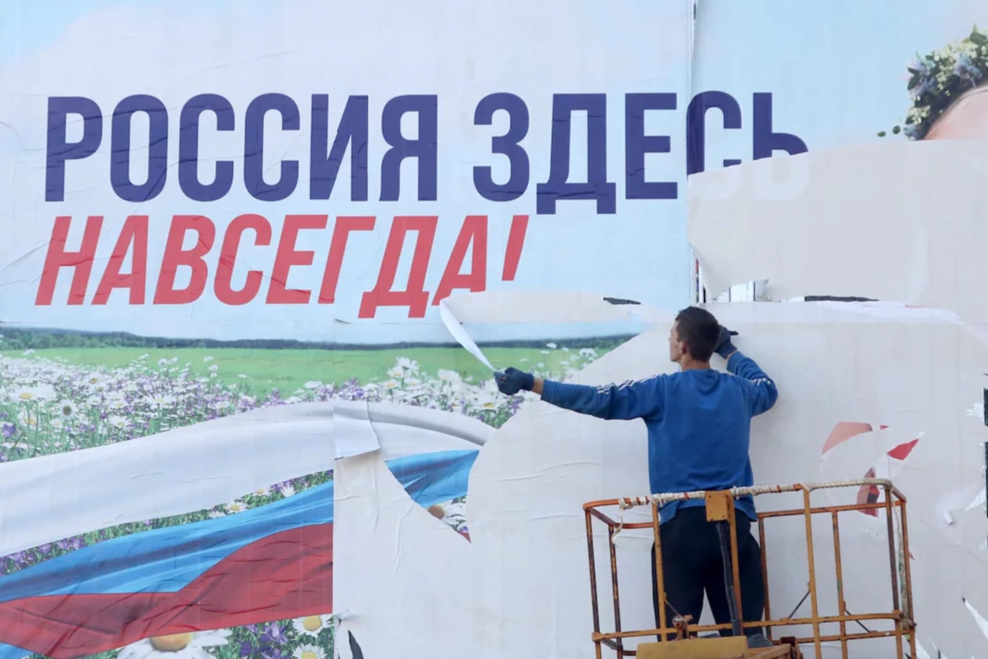 <p>A Ukrainian tears down a billboard reading “Russia is here forever” in Kherson, Ukraine, on Monday. </p>
