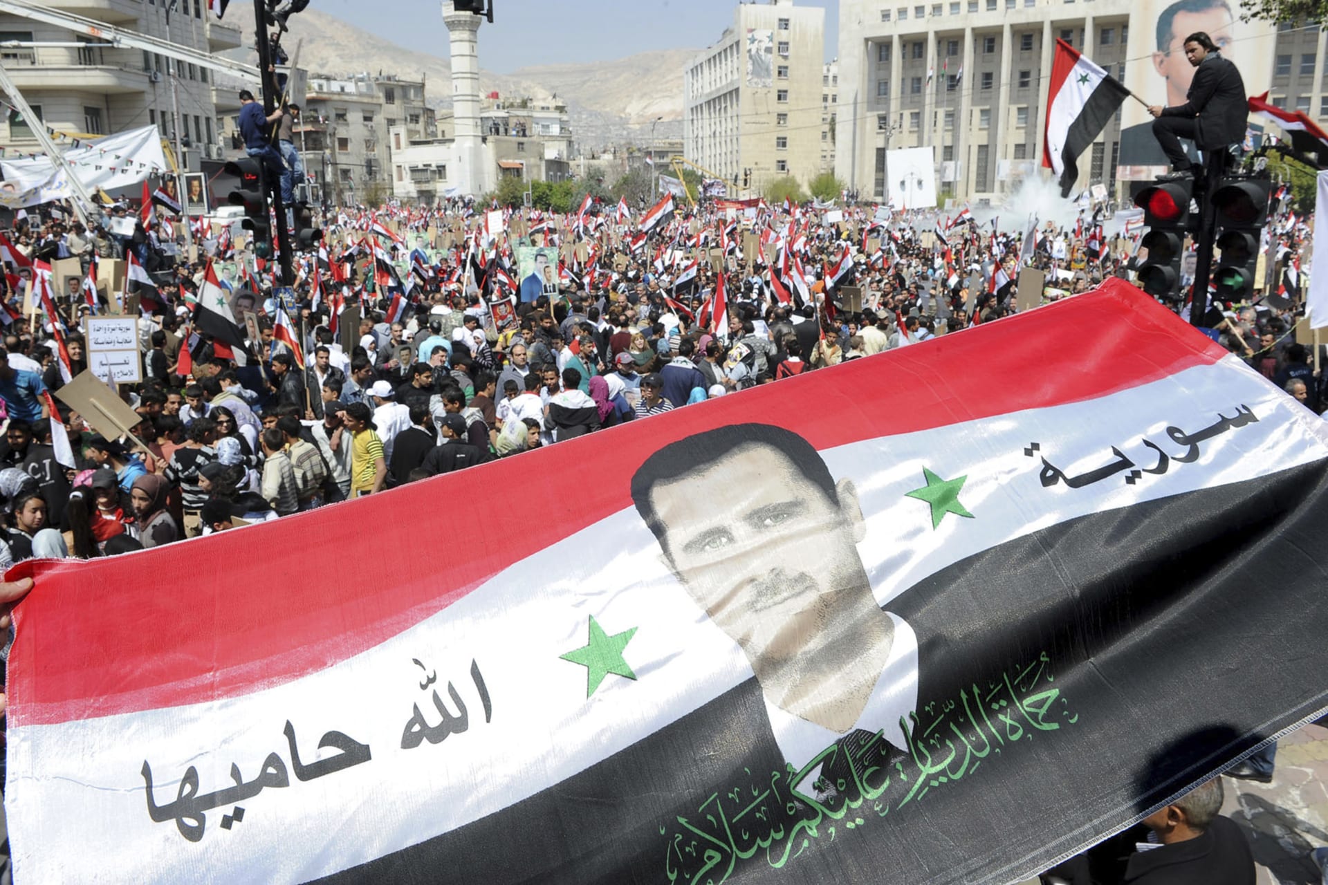<p>Syrians display a giant national flag with a picture of Syria’s President Bashar al-Assad during a pro-government rally in 2011. (STRINGER/REUTERS)</p>
