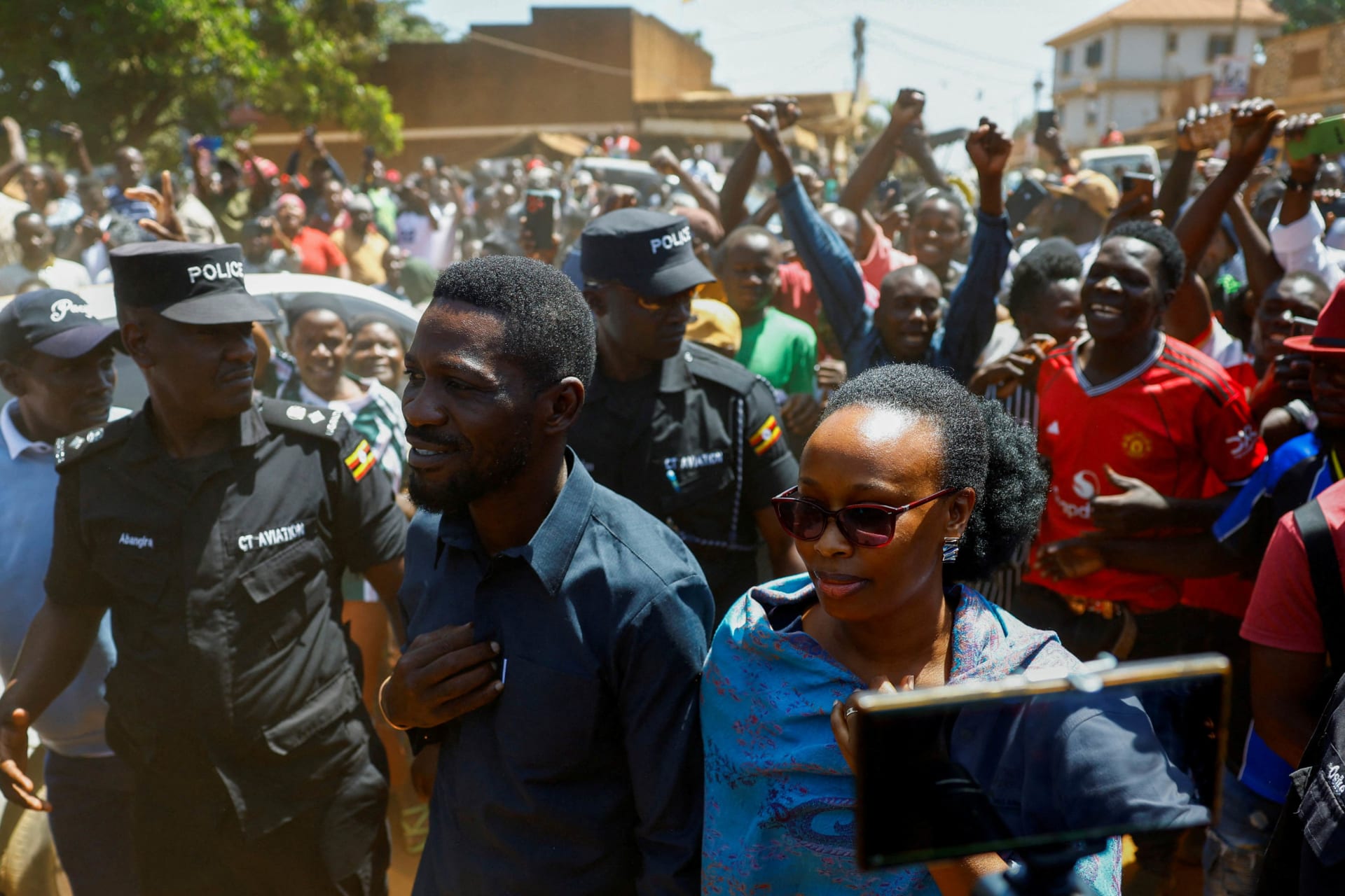 <p>Ugandan presidential candidate Robert Kyagulanyi (Bobi Wine), of the National Unity Platform party, flanked by his wife Barbara Kyagulanyi, are escorted by police and supporters as they arrive to cast their votes in the general election, within the Magere neighborhood of the Kasangati district in Kampala, Uganda, on January 15, 2026.</p>
