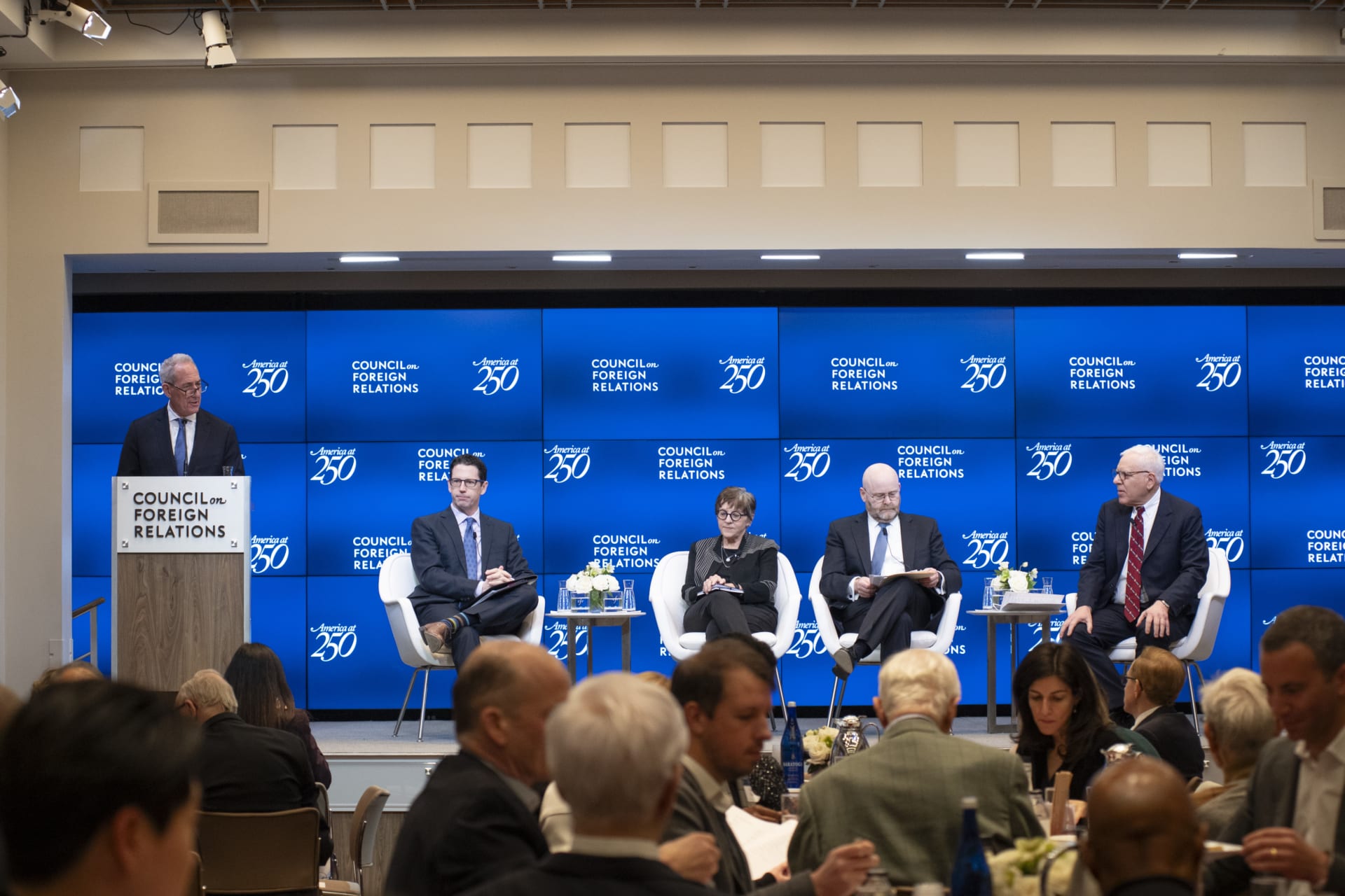 Photograph of CFR President Michael Froman standing at a lectern with four other men sitting on a raised stage in front of a blue screen with CFR logos displayed.