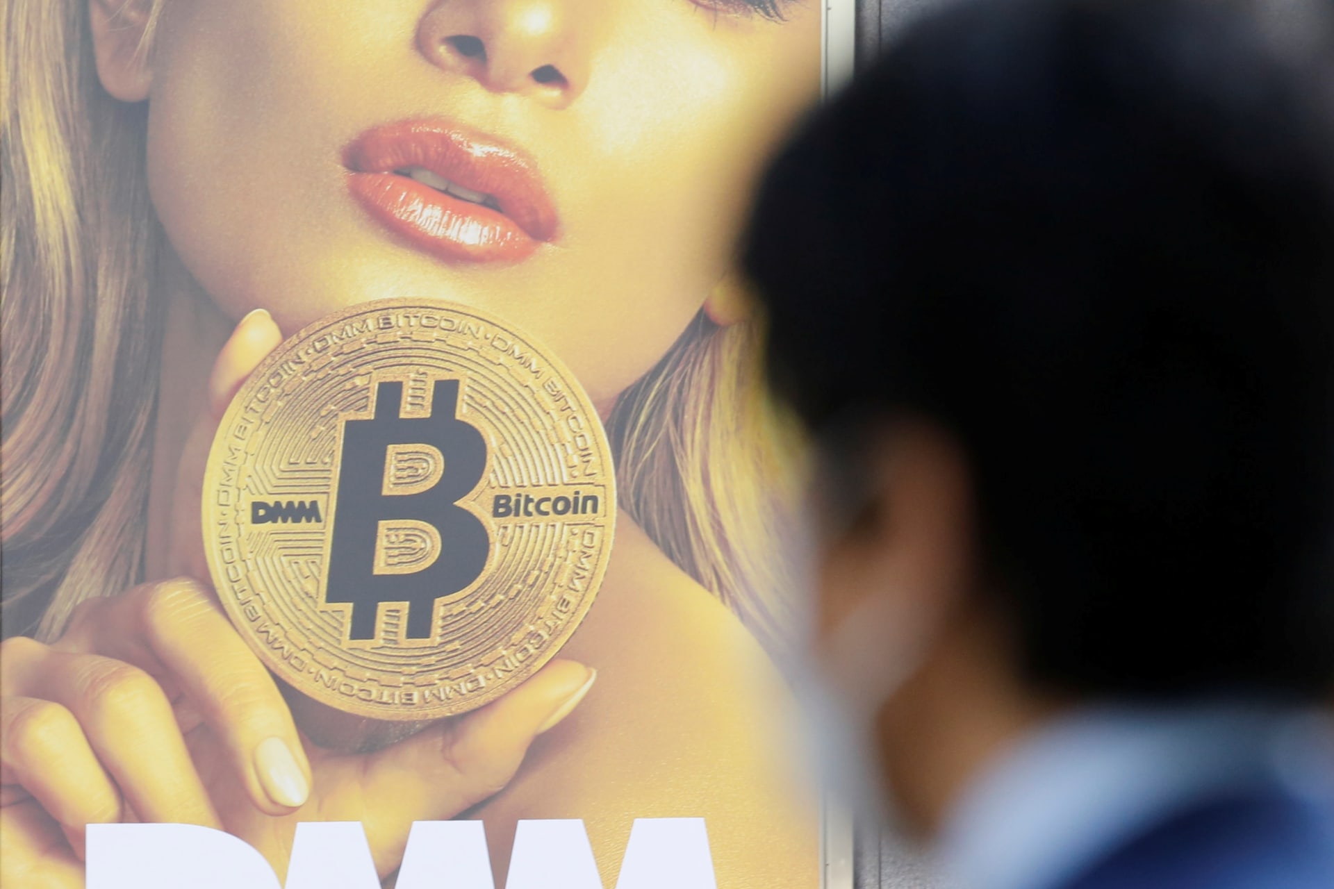 <p>A man stands near an advertisement of a cryptocurrency exchange in Tokyo, Japan.</p>

