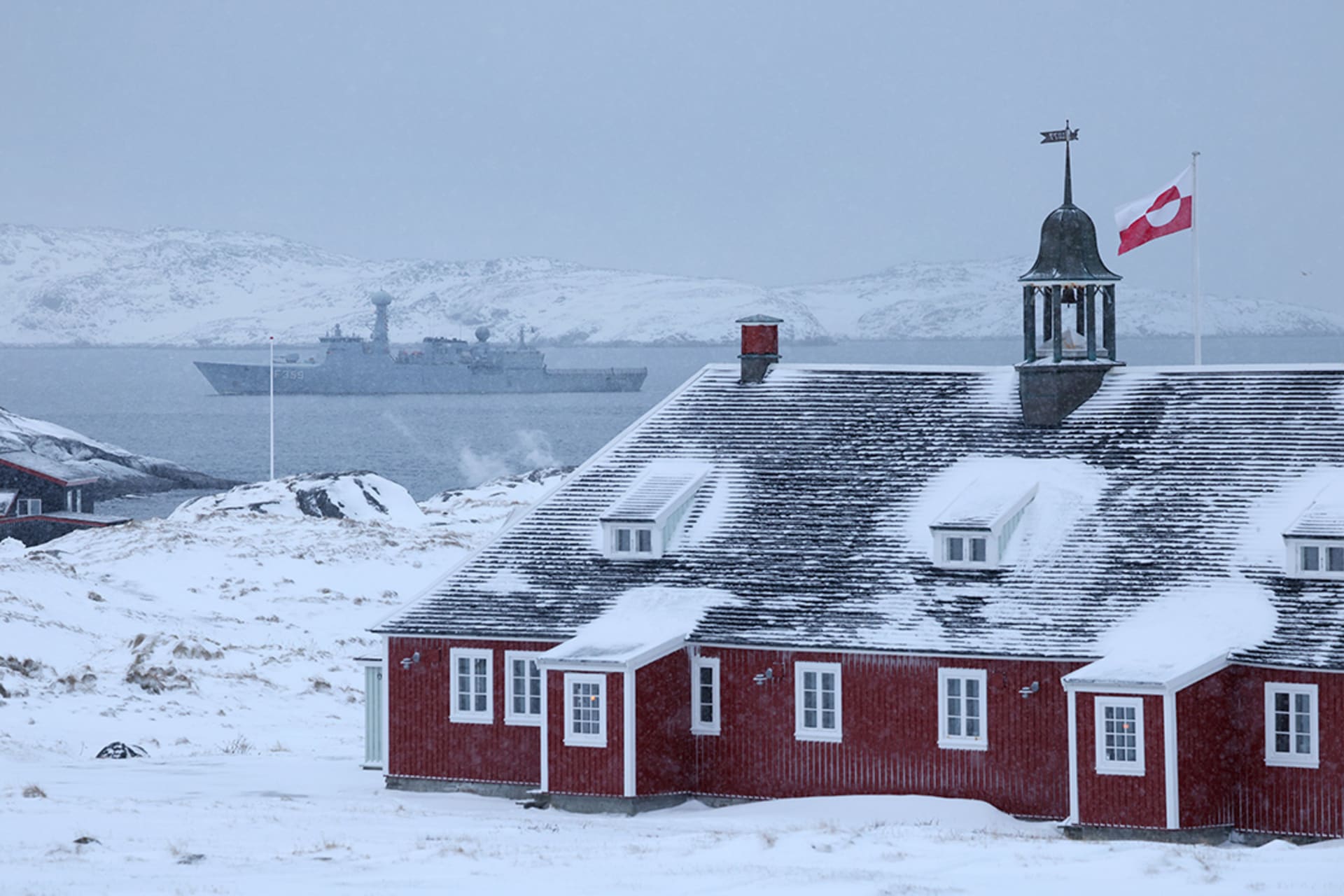 <p>The Greenlandic flag flies over a building as the HDMS Vaedderen frigate of the Danish Navy patrols behind in Nuuk, Greenland on January 18, 2026</p>
