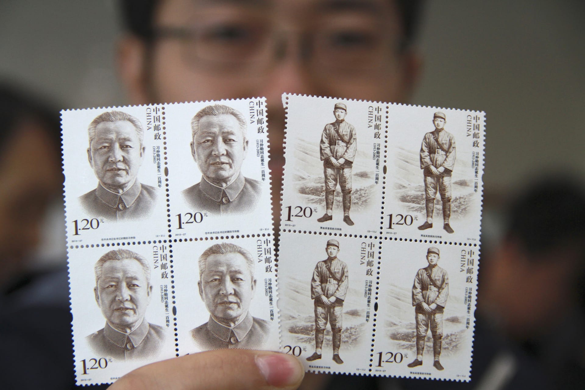 A man poses for pictures as he holds postage stamps of Xi Zhongxun, China's former vice premier and father of China's President Xi Jinping, in Yantai