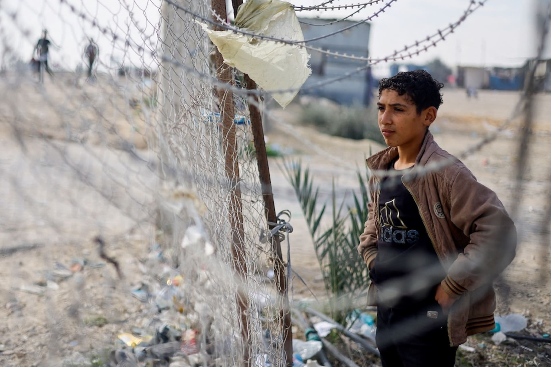 <p>A boy stands next to a fence as displaced Palestinians who fled their homes due to Israeli strikes shelter at Rafah crossing on the border with Egypt, amid the ongoing conflict between Israel and the Palestinian Islamist group Hamas, in Rafah in the southern Gaza Strip, December 8, 2023. </p>
