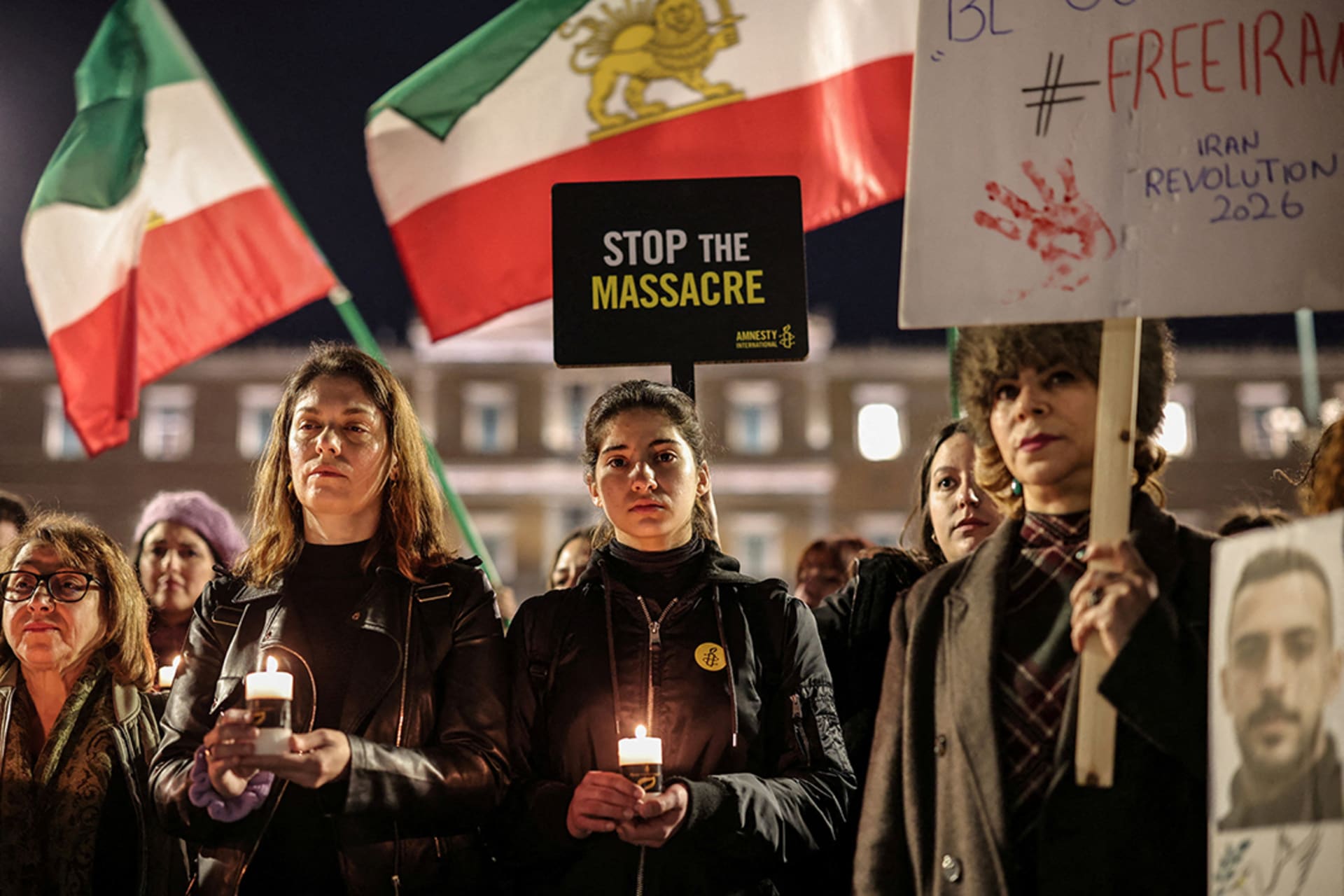 Activists stand in a line holding Iranian flags, candles, and signage to peacefully protest the Iranian crackdowns on civilian demonstrations in front of the Greek Parliamentary building.