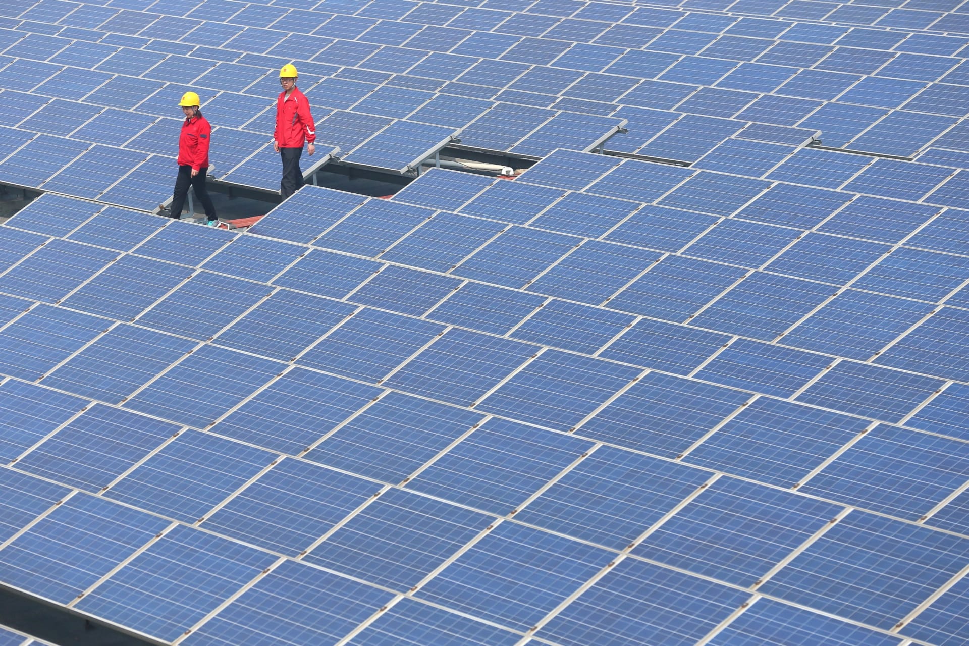 Workers walk past solar panels in Jimo, Shandong Province, China