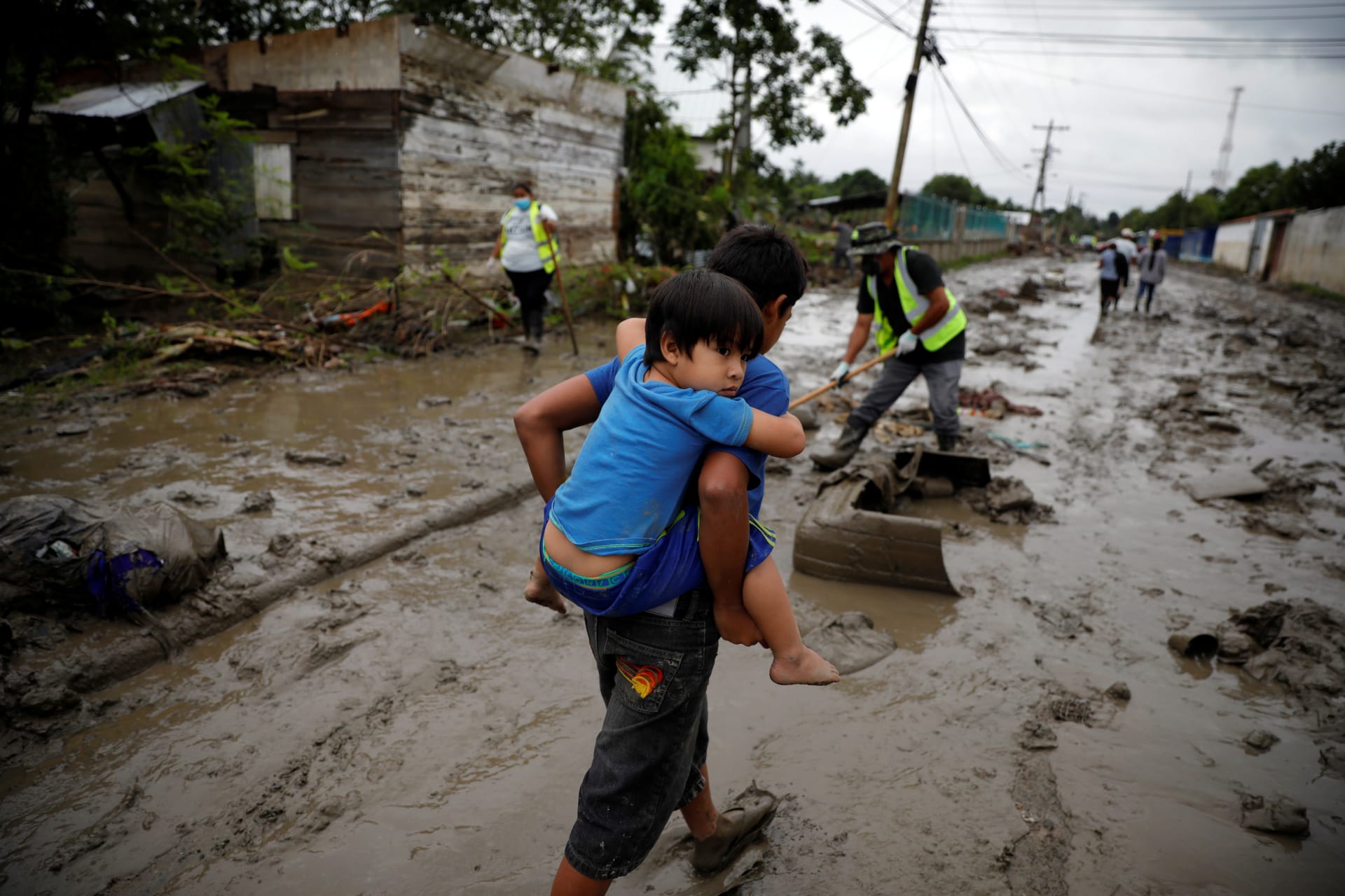 A child carries his brother in a street covered in mud after the floods caused by the rains brought by Hurricanes Eta and Iota, in La Lima