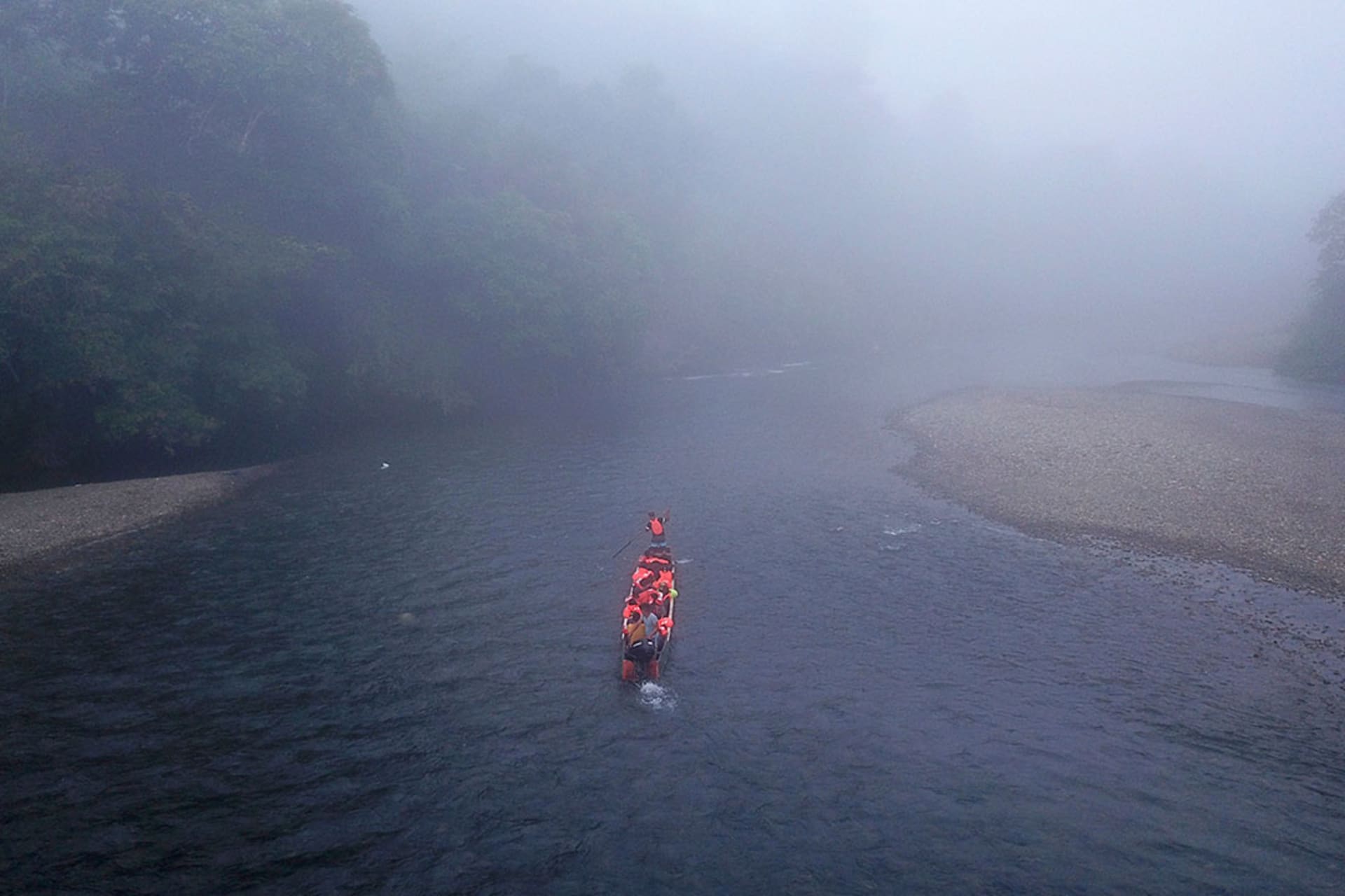 View of small boat, navigating through fog on a river, transporting migrants.