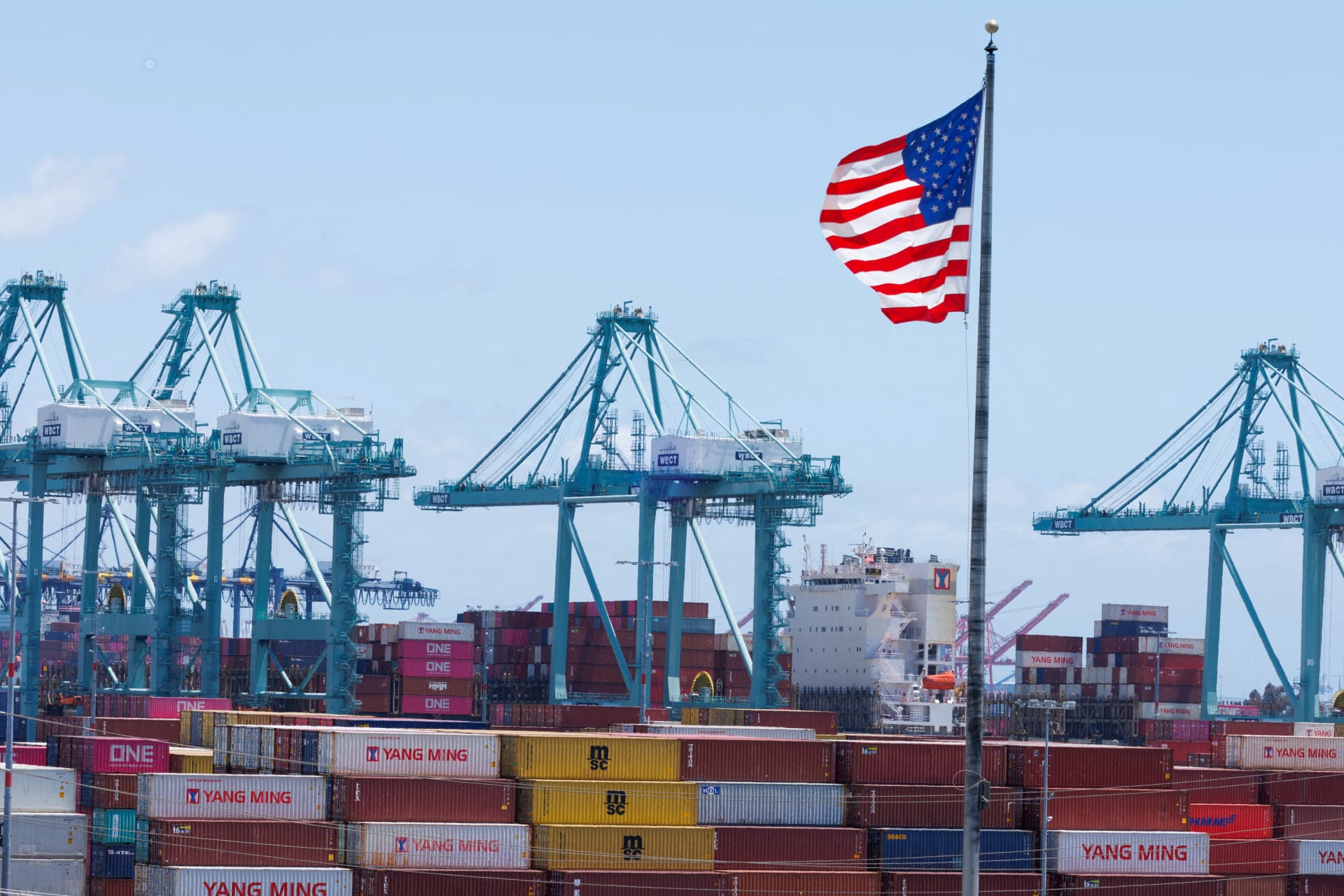 An American flag flutters over a ship and shipping containers at the Port of Los Angeles, in San Pedro California, U.S., May 13, 2025. REUTERS/Mike Blake/File Photo