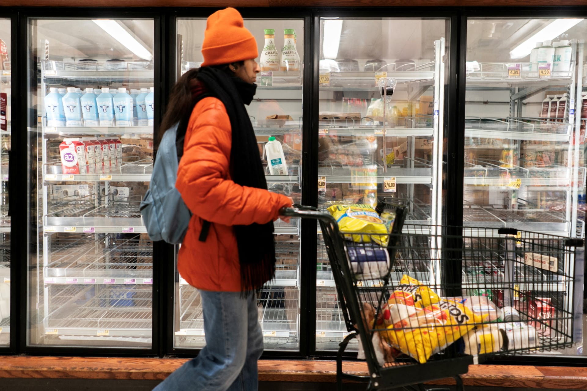 A shopper walking past a partially empty dairy section of a grocery store