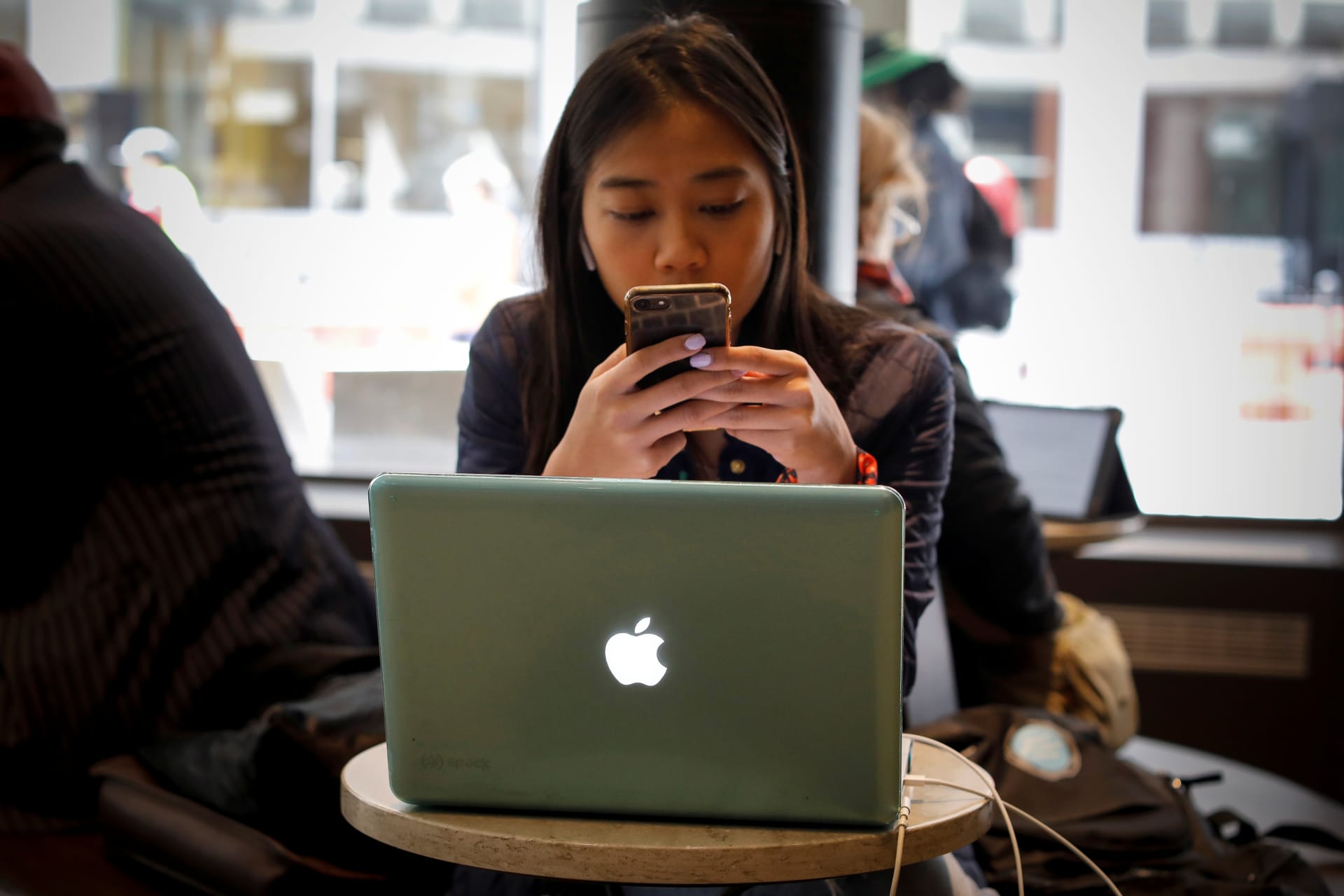 <p>A woman uses her Apple iPhone and laptop in a cafe in lower Manhattan in New York City</p>

