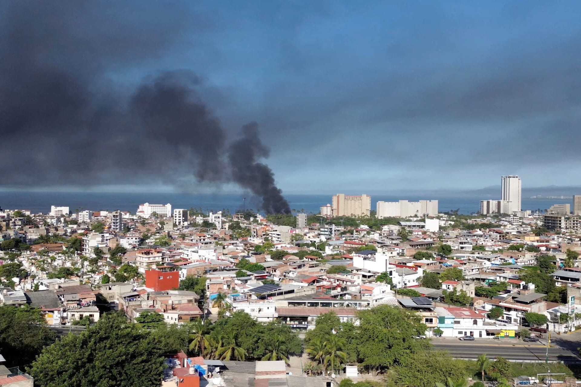 Smoke billows from an urban area by the sea.