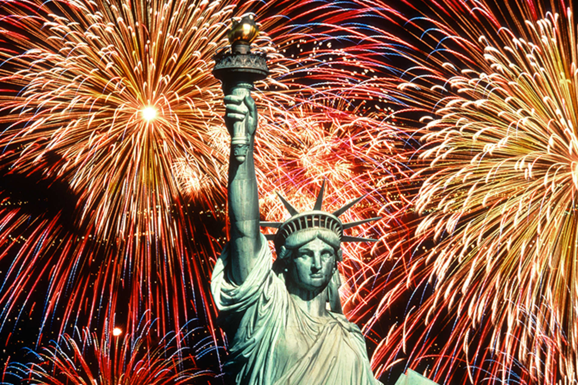 The statue of liberty backlit by fireworks in the night sky.