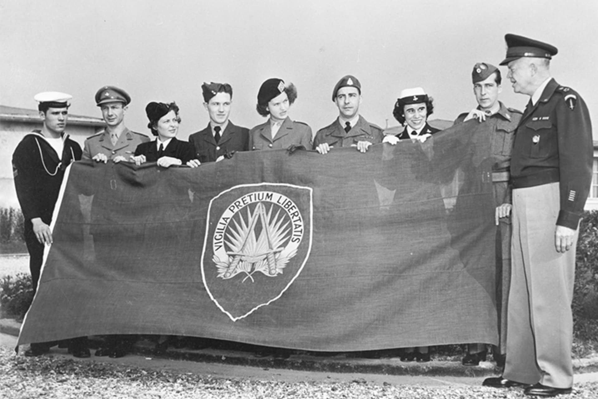 A black and white photo of General Dwight D. Eisenhower and members of the UN holding the first NATO flag. 