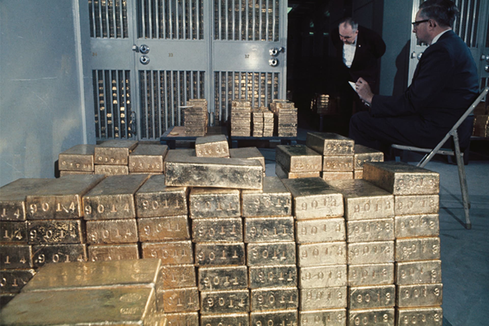 A photo of two men counting lots of gold bars in a basement. 