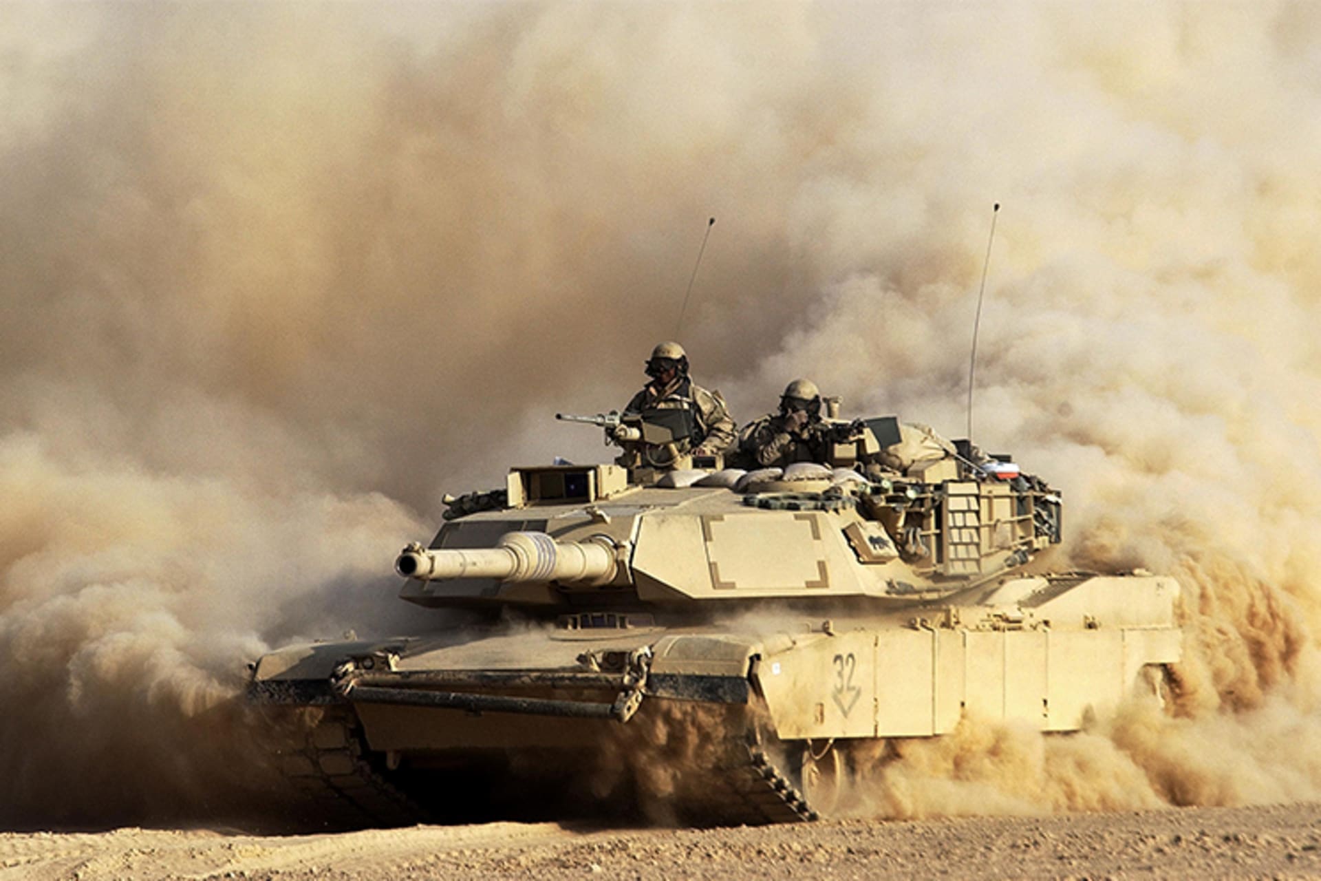 A photo of a U.S. tank rolling into Iraqi territory. The tank is kicking up lots of dust all around.