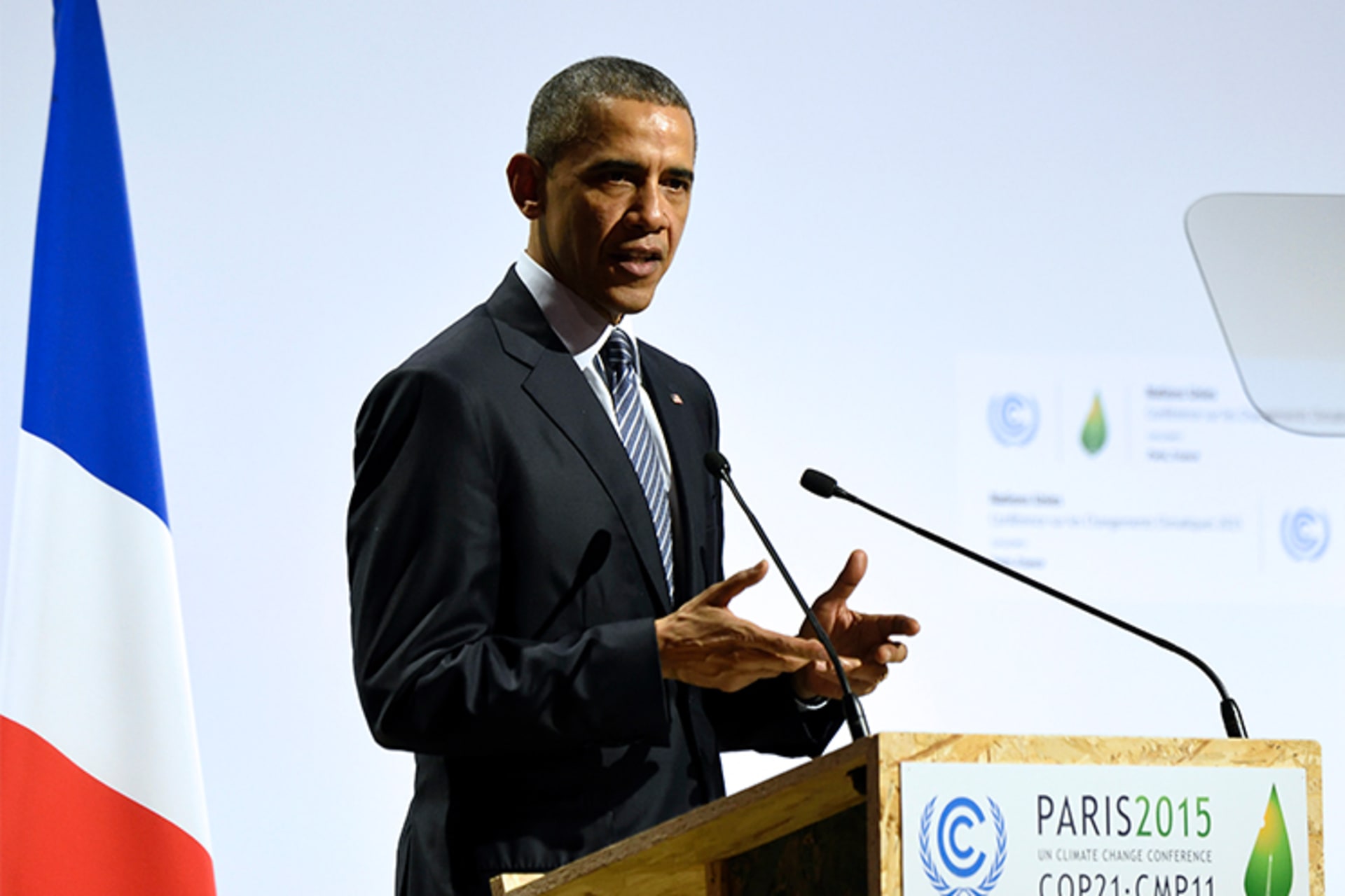 A photo of President Barack Obama speaking at a podium at the COP 21 UN conference while a French flag stands behind him.
