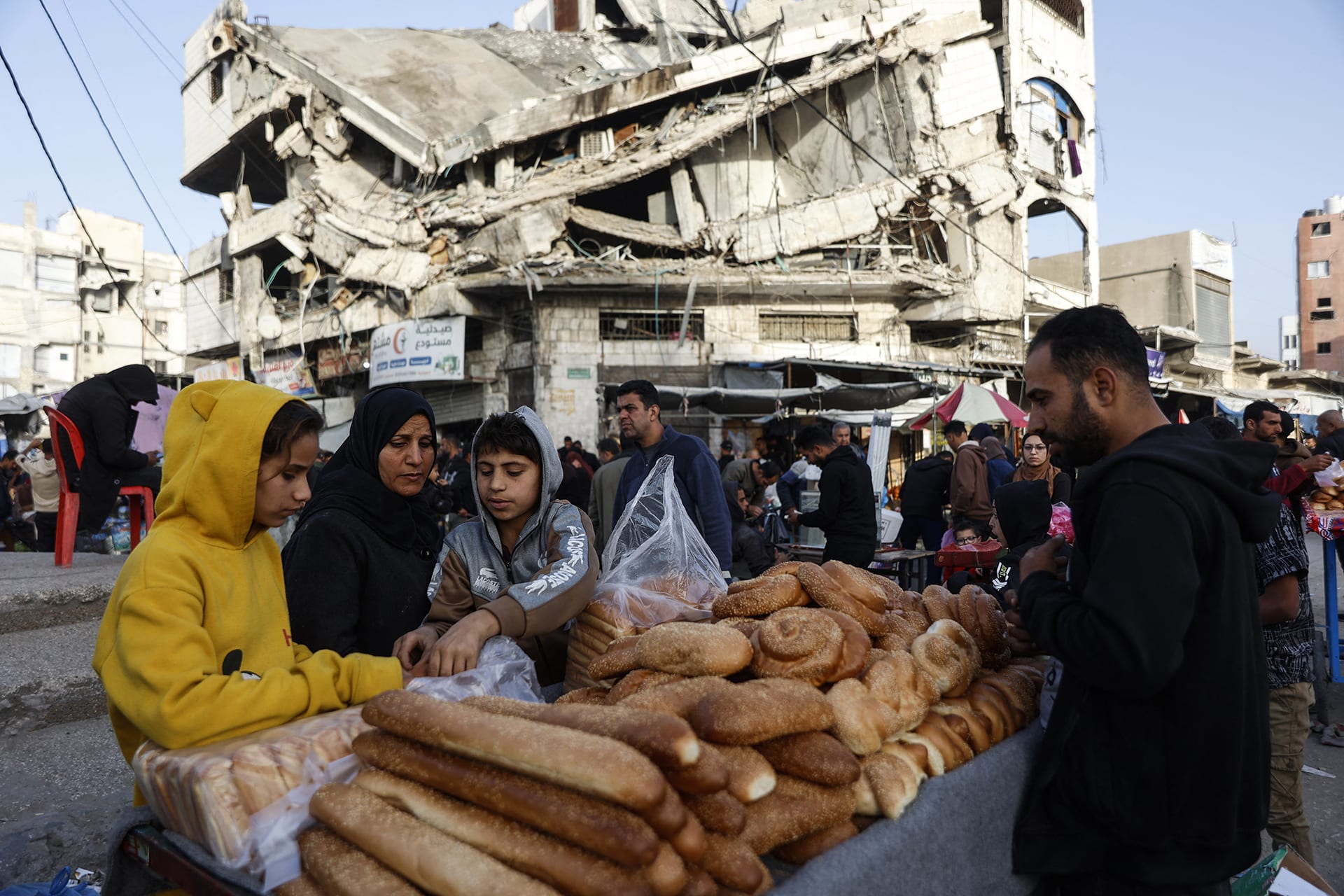 Palestinians sell bread on a street beneath a destroyed building in Gaza City's Zawiya market on February 18, 2026, on the first days of the holy fasting month of Ramadan.