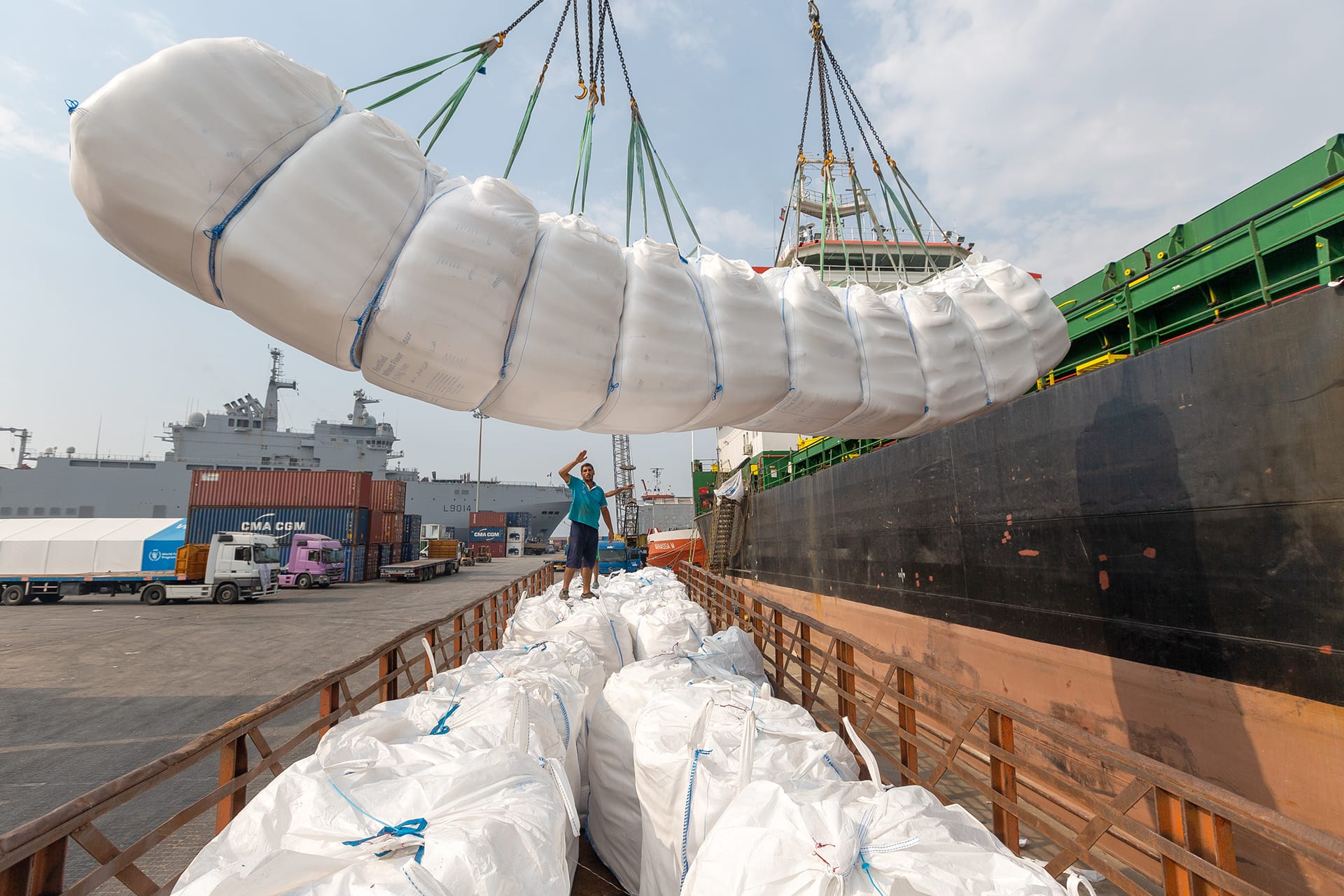 A crane lowers a white package containing food aid into a crate off of the side of a ship.
