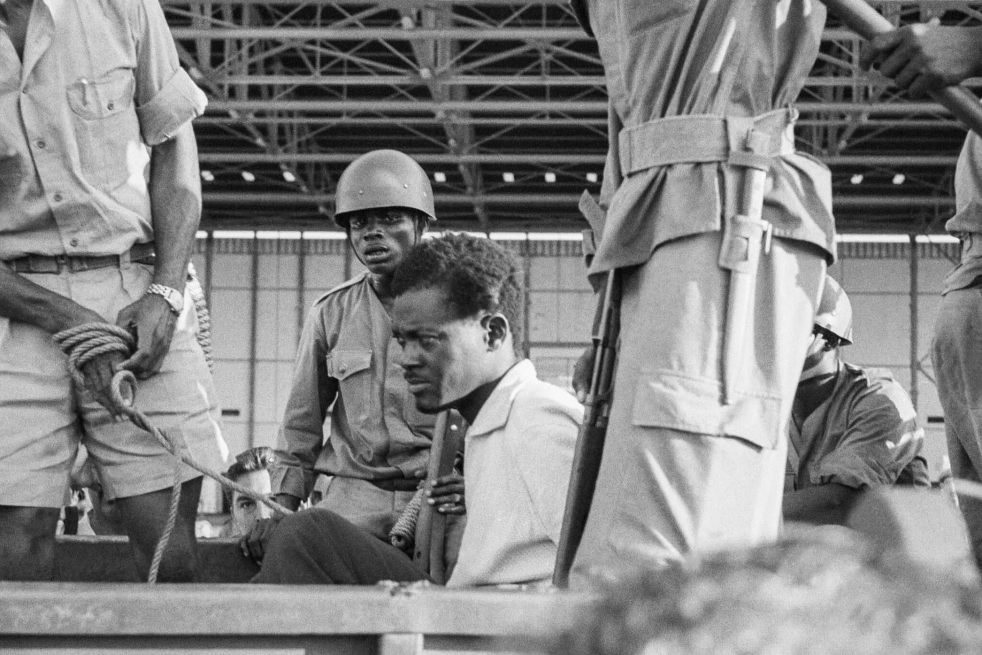 A man sitting in the bed of a truck surrounded by men in military garb_