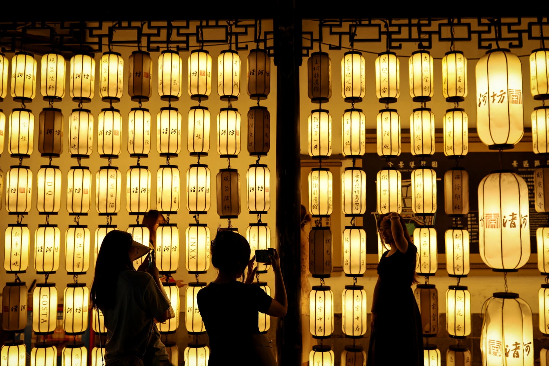 Photograph of silhouetted figures standing in front of a wall of lit laterns.