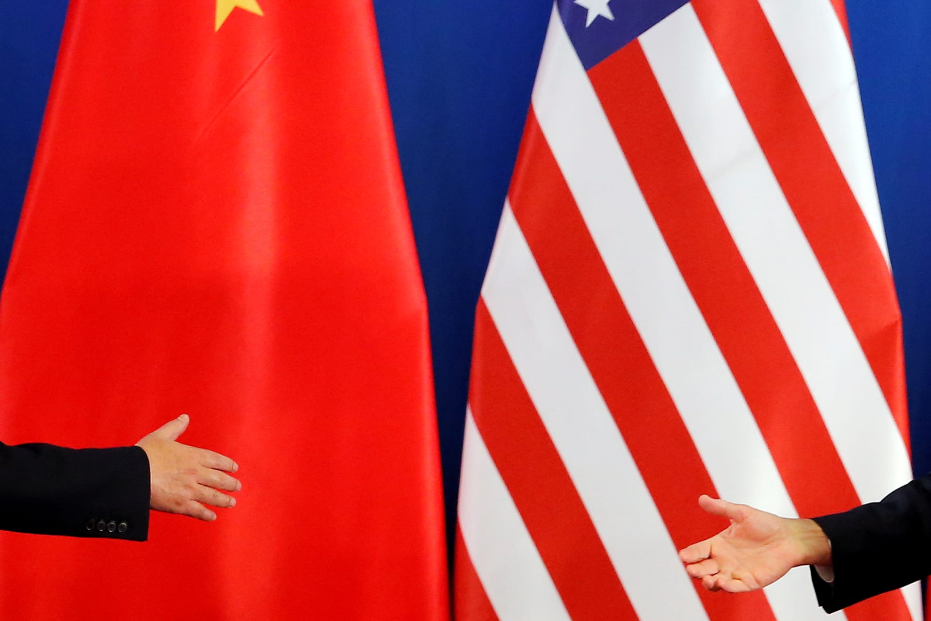 Photograph with a Chinese and an United States of America flag with two hands reaching out to shake.