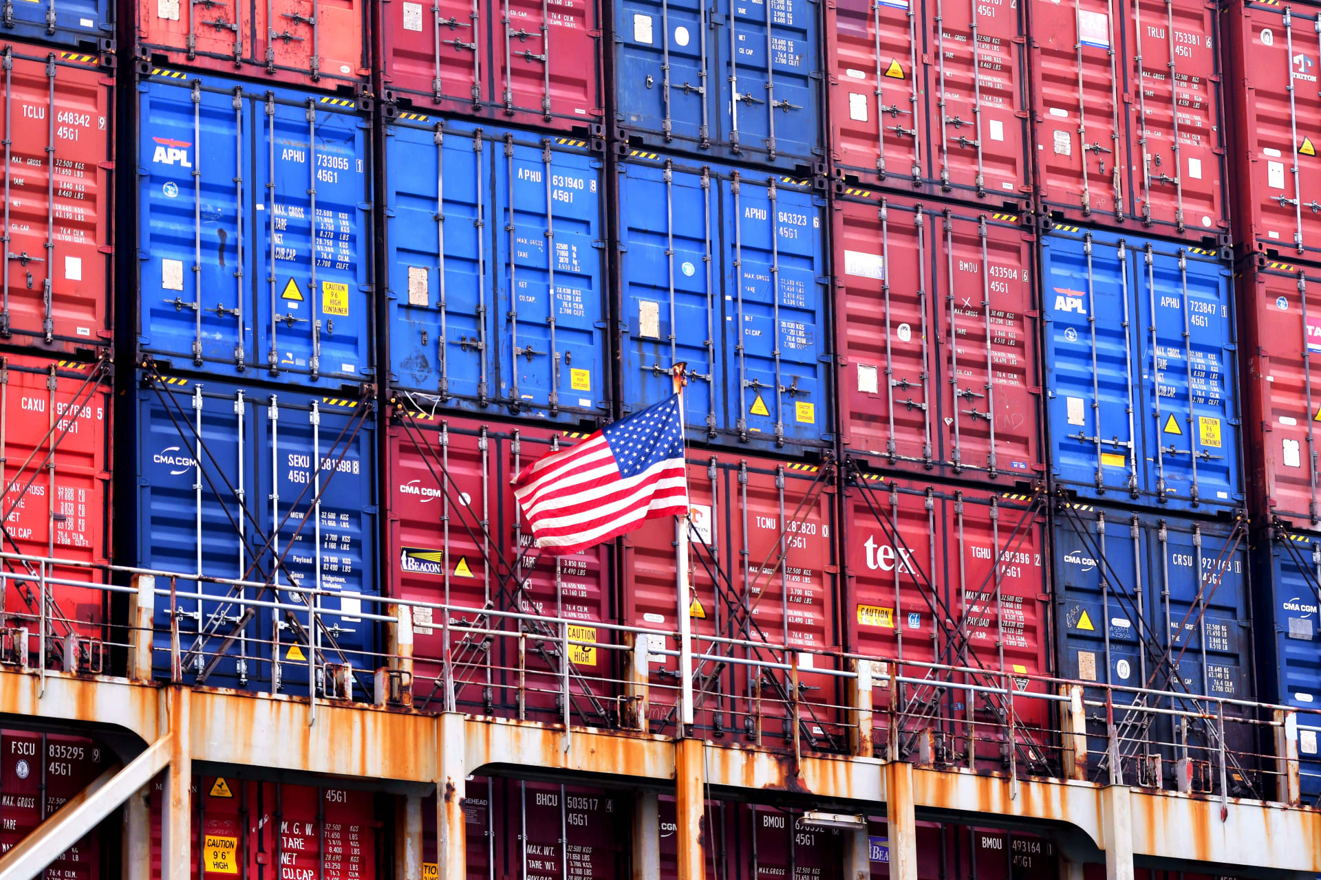 Photograph of a wall of blue and red shipping containers with an American flag in front.