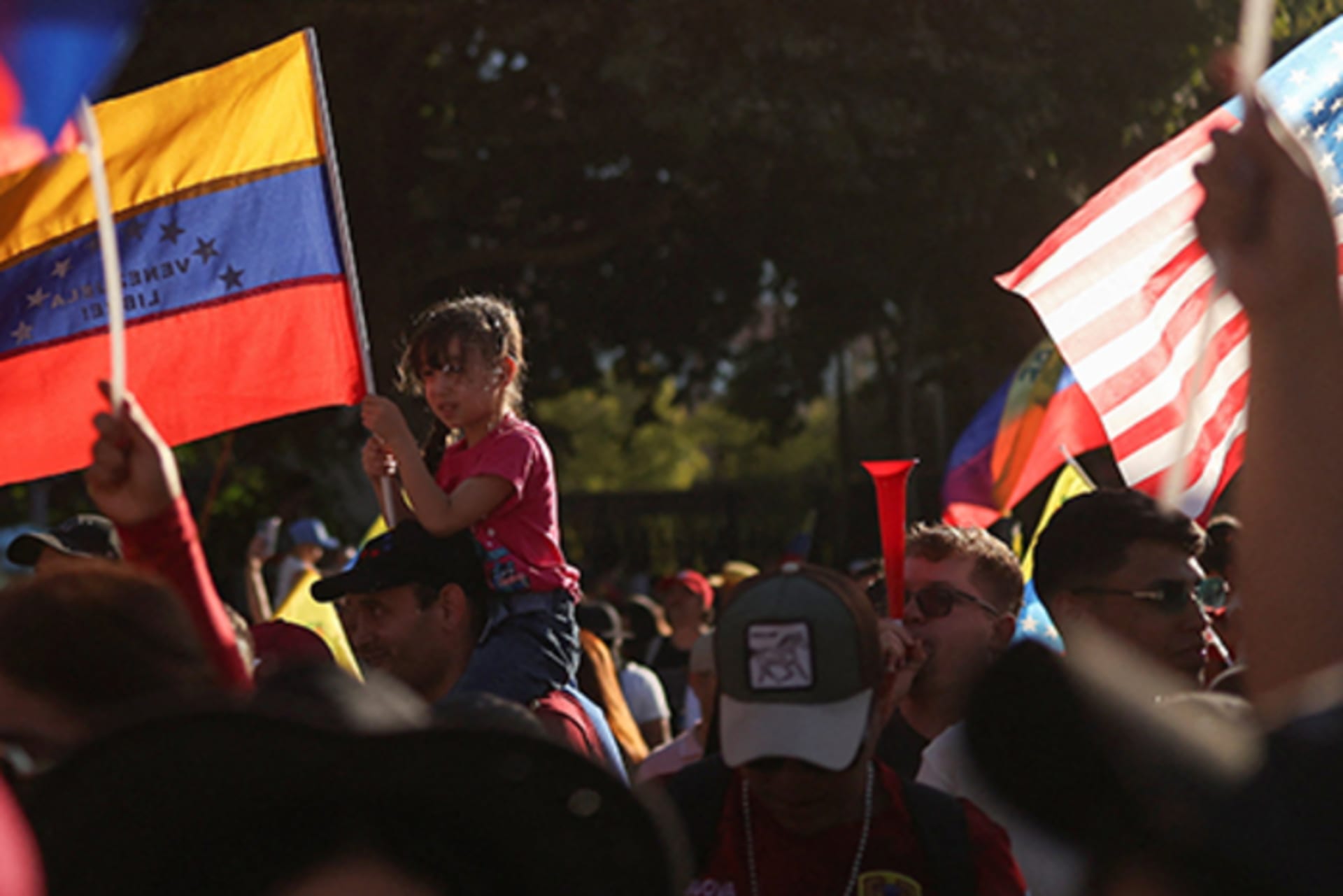 A girl holds a Venezuelan flag as others around her raise Venezuelan and American flags