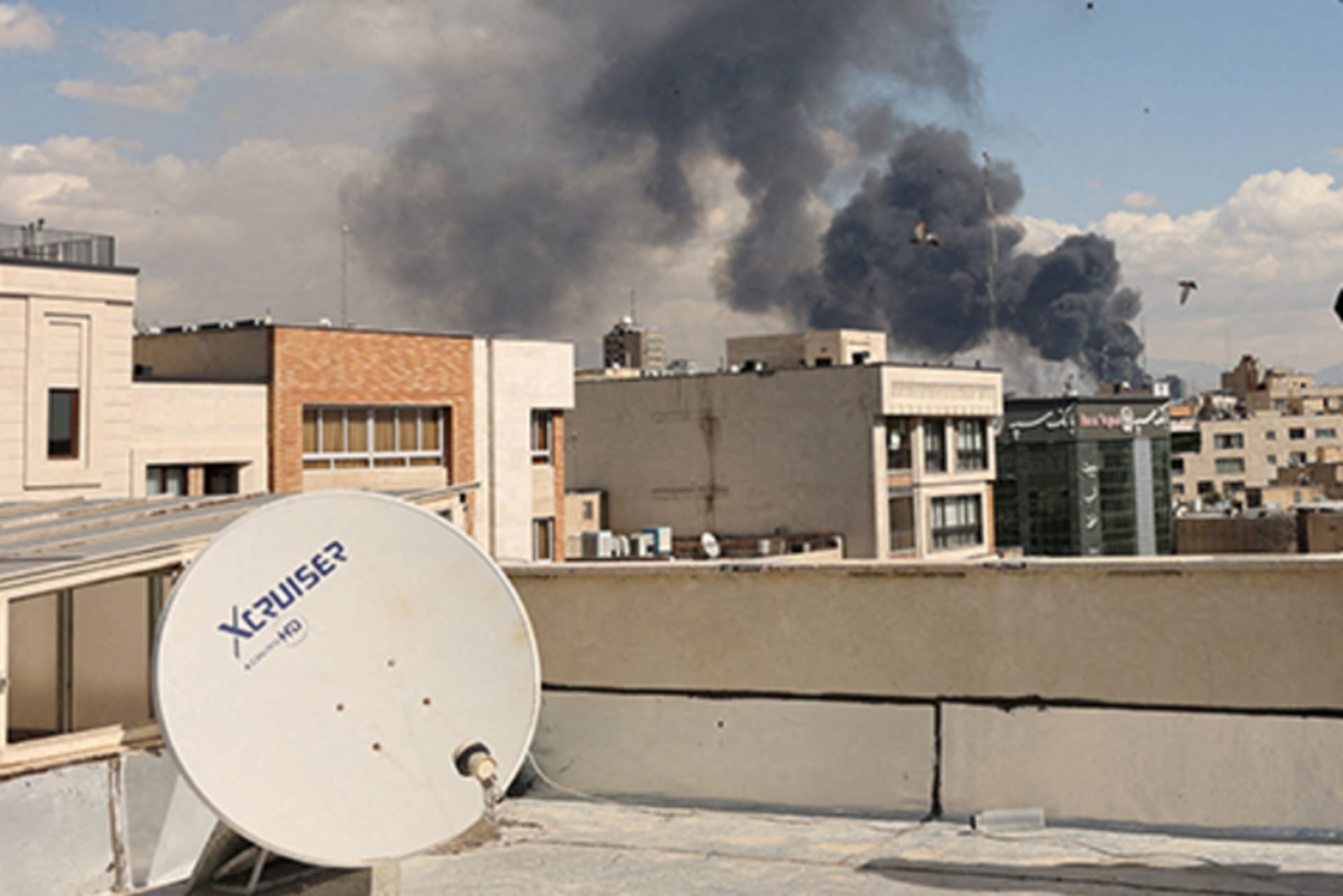 woman watches smoke rise above buildings after missile attacks in Tehran