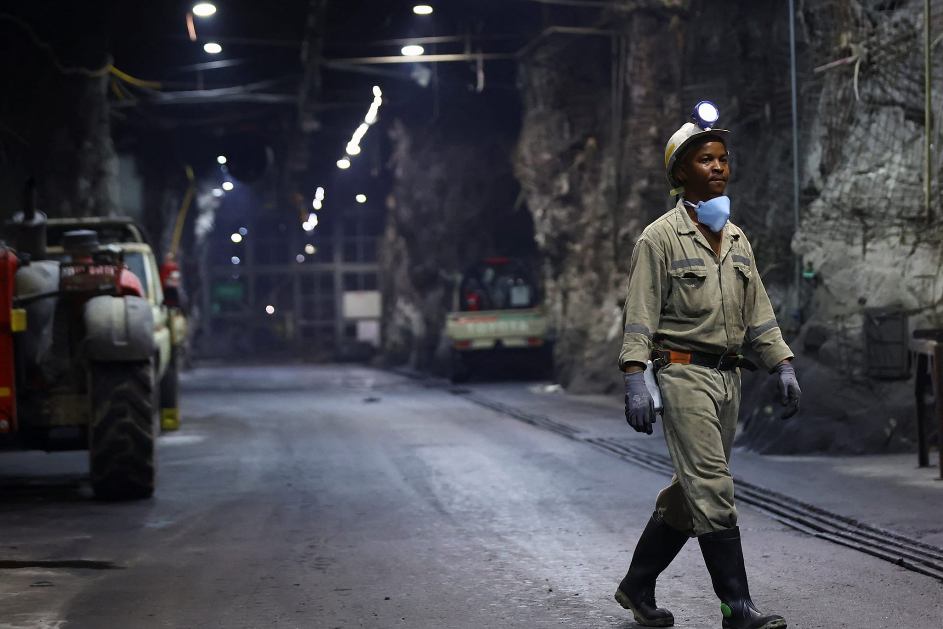 A mine worker in uniform, with a flashlight on their head, walks underground at Gold Fields' South Deep mine.