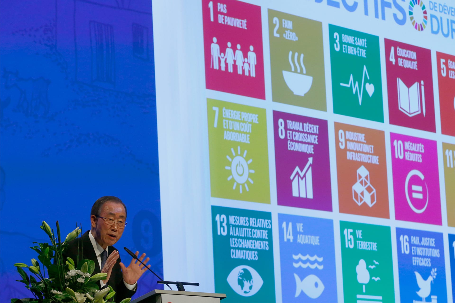 Ban Ki-Moon speaking at a podium in front of large screen featuring icons for the 17 SDGs