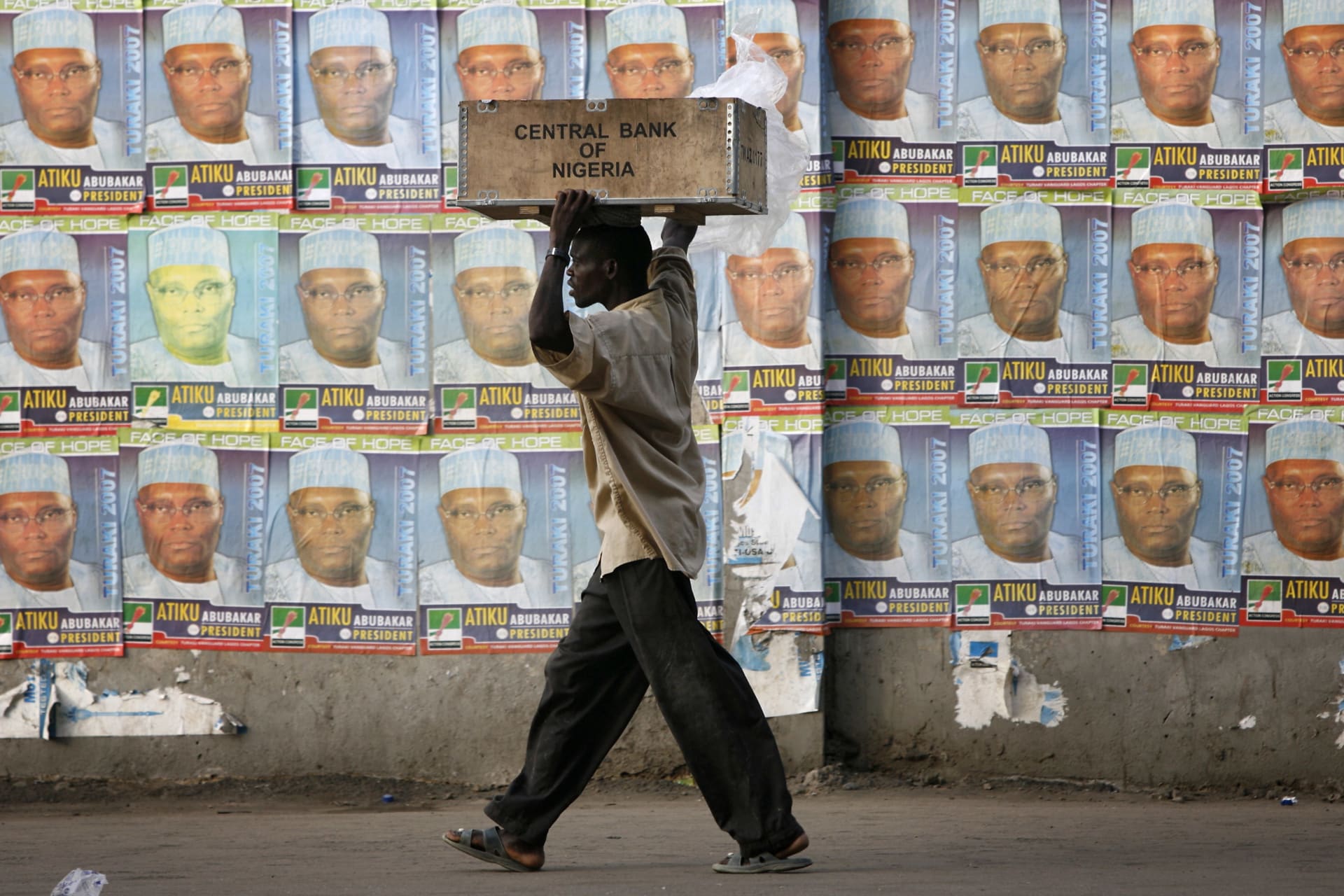 <p>A laborer passes in front of a wall plastered with election posters for then-presidential hopeful Atiku Abubakar in Nigeria’s commercial capital Lagos, on April 12, 2007.</p>
