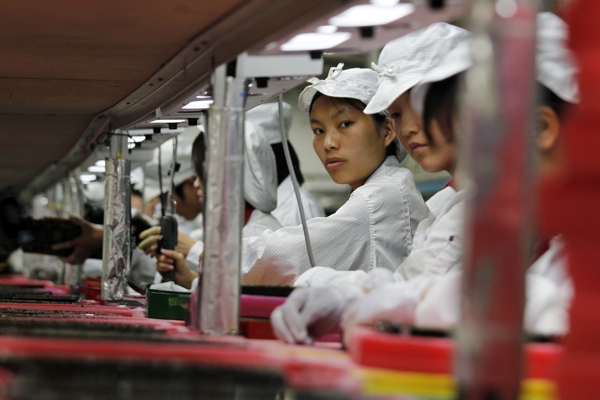 Chinese workers in white uniforms are seen working on an assembly line inside a factory.