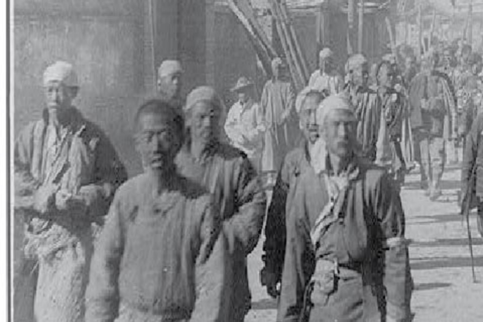 Black and white photo of Chinese men walking in dirt street circa 1901.