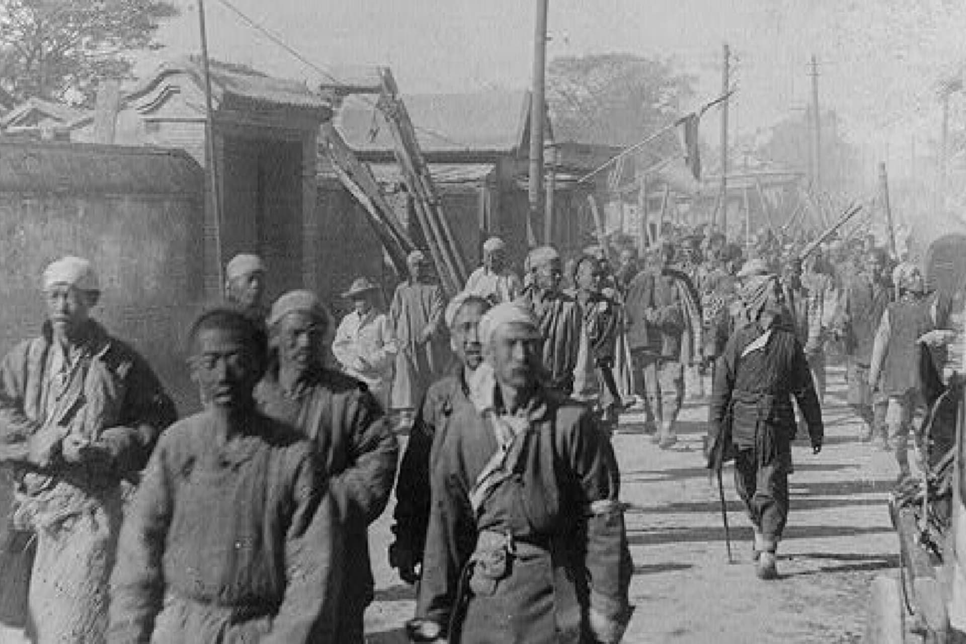 Black and white photo of Chinese men walking in dirt street circa 1901.