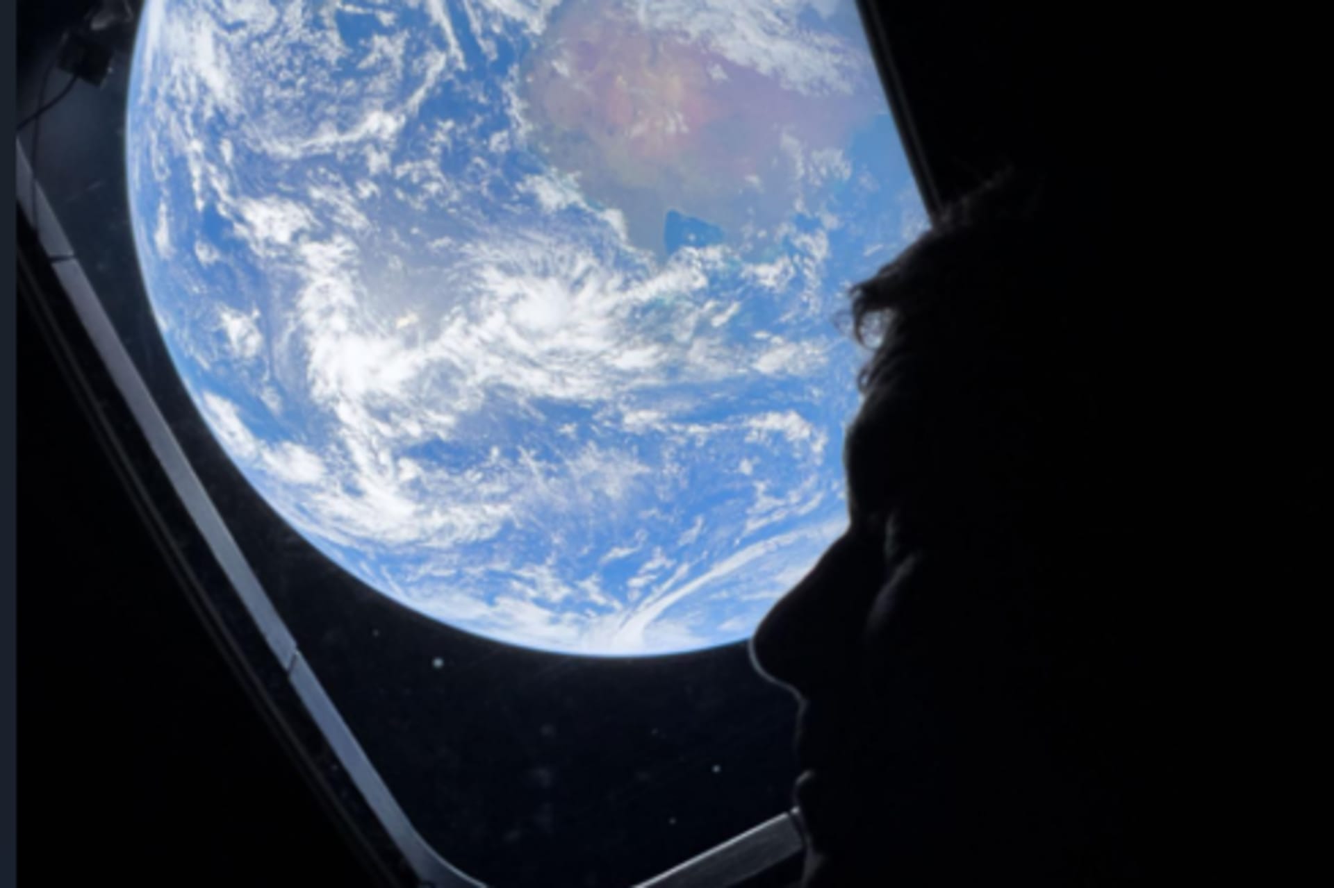 NASA astronaut and Artemis II Commander Reid Wiseman peers out of one of the Orion spacecraft's main cabin windows, looking back at Earth, as the crew travels towards the Moon.