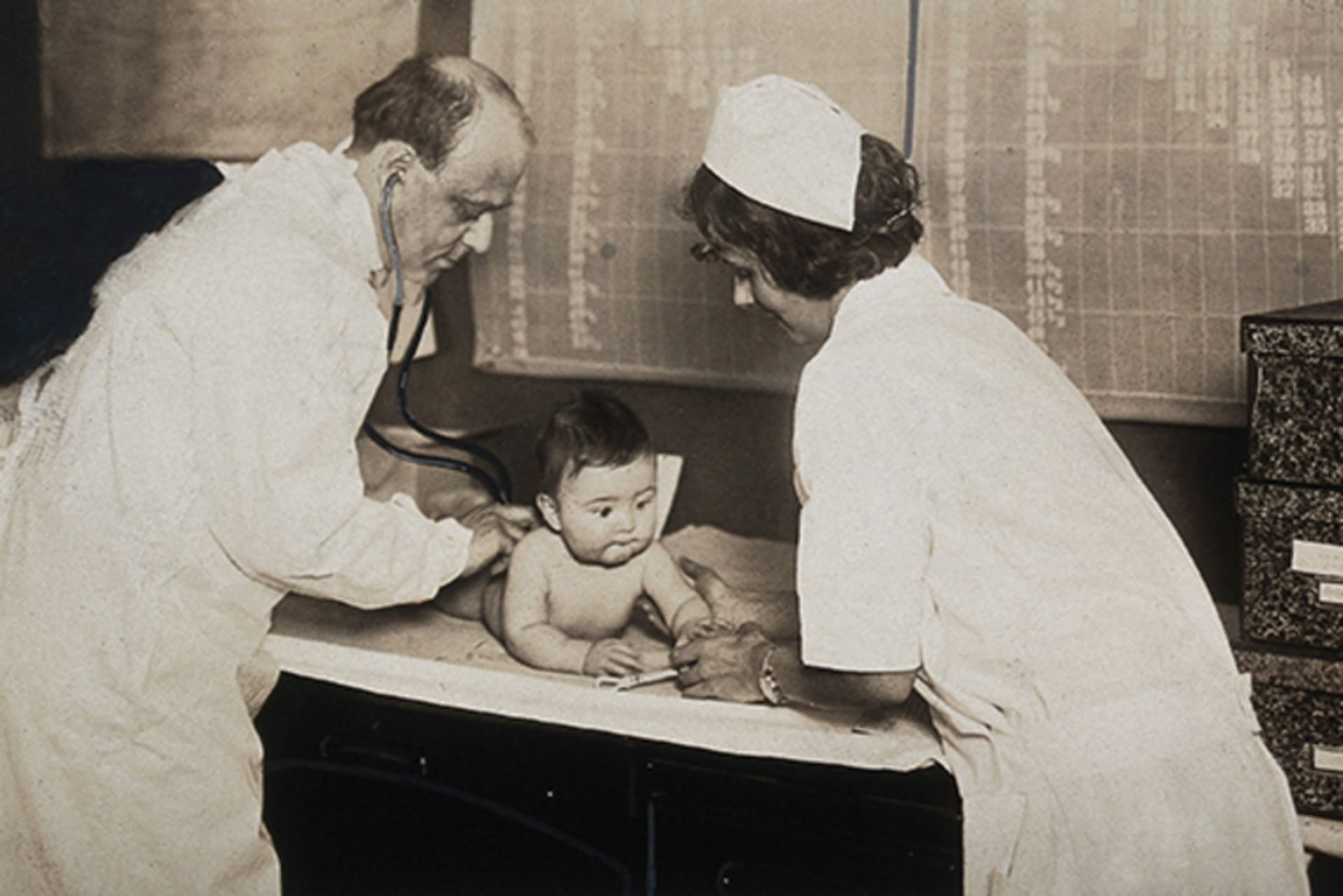 A baby is examined by a nurse and a doctor with a stethoscope at a state baby clinic in Pennsylvania, circa 1925.