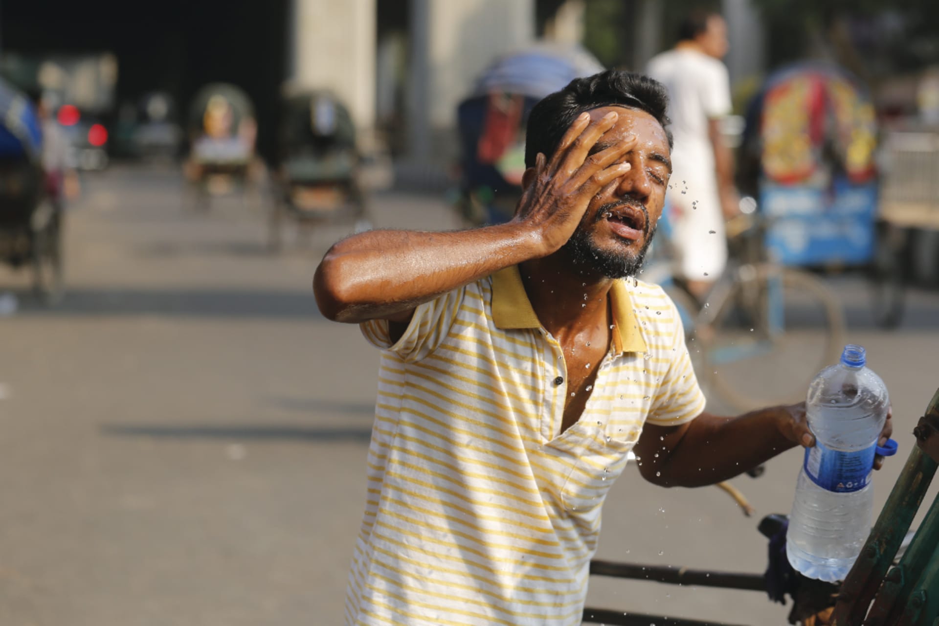 A rickshaw driver splashes water from a water bottle on his face to find relief from the intense heatwave in Dhaka, Bangladesh.