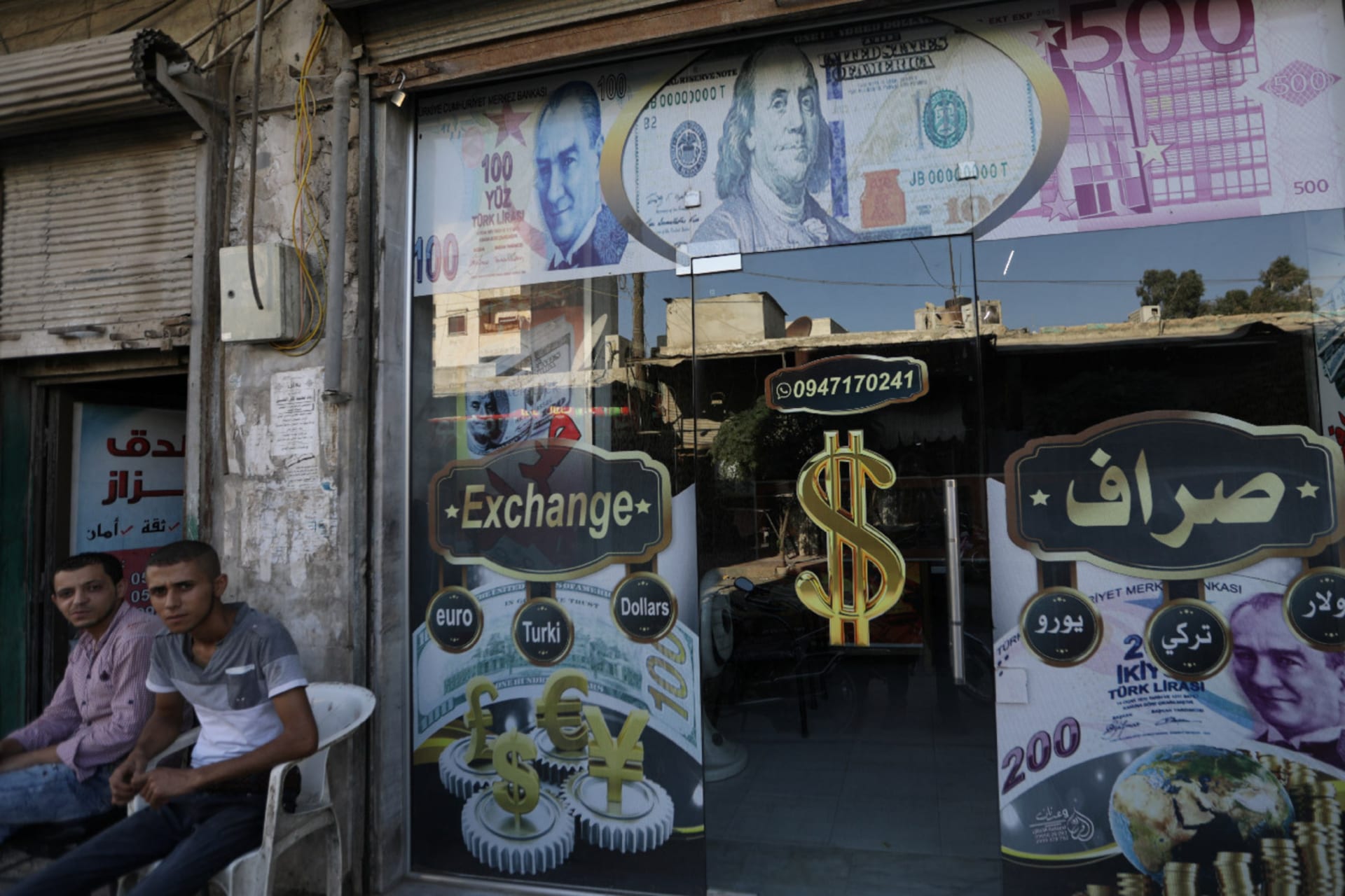Two men sit outside a currency exchange shop decorated with posters of the U.S. dollar and Turkish lira in the city of Azaz, Syria.